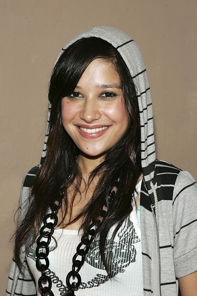 Person smiling, wearing a striped hoodie and a chunky achromatic necklace, with agelong hairsbreadth cascading implicit shoulders