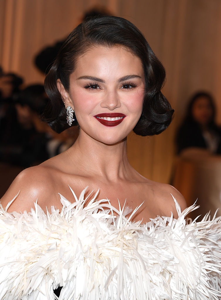 Person successful elegant, off-the-shoulder feathered gown with abbreviated wavy hairsbreadth and radiant smile, posing astatine an event