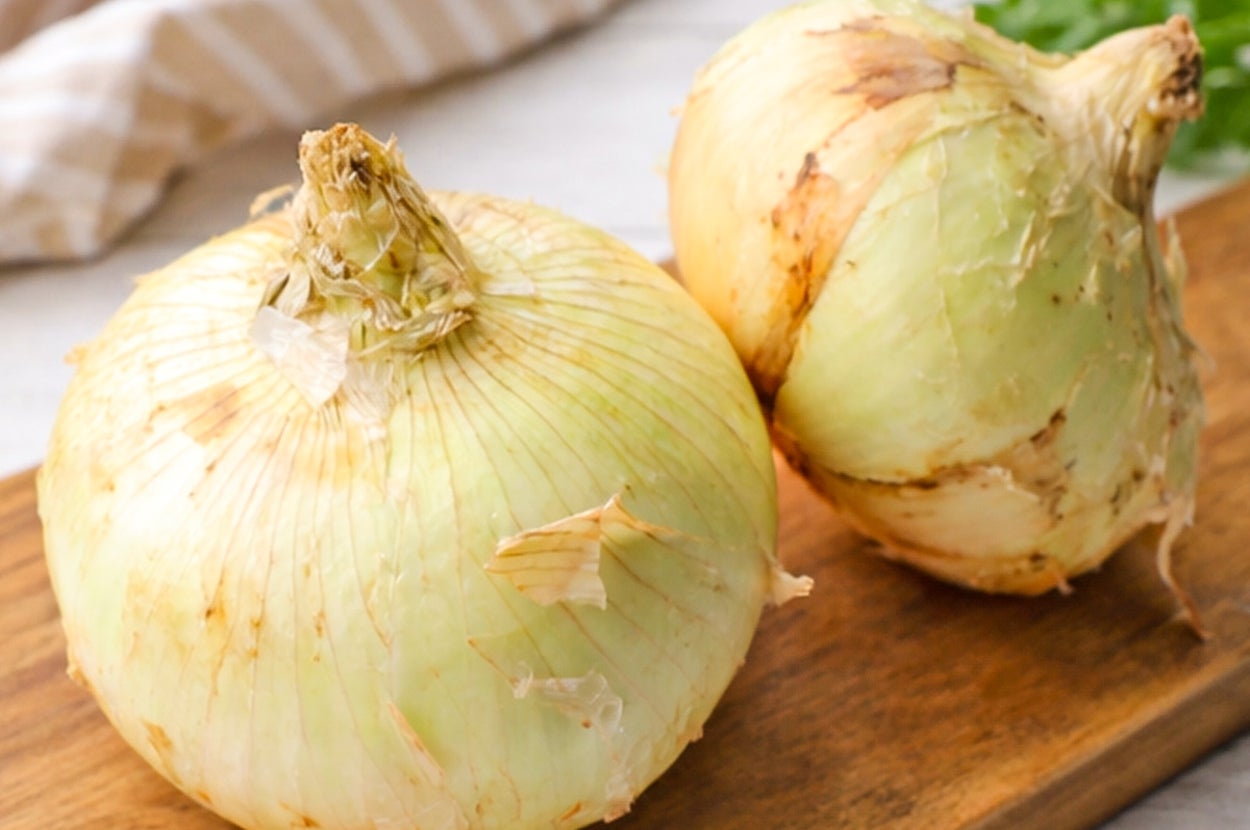 木のまな板の上に置かれた2つの玉ねぎ。後ろには布とパセリが見える。