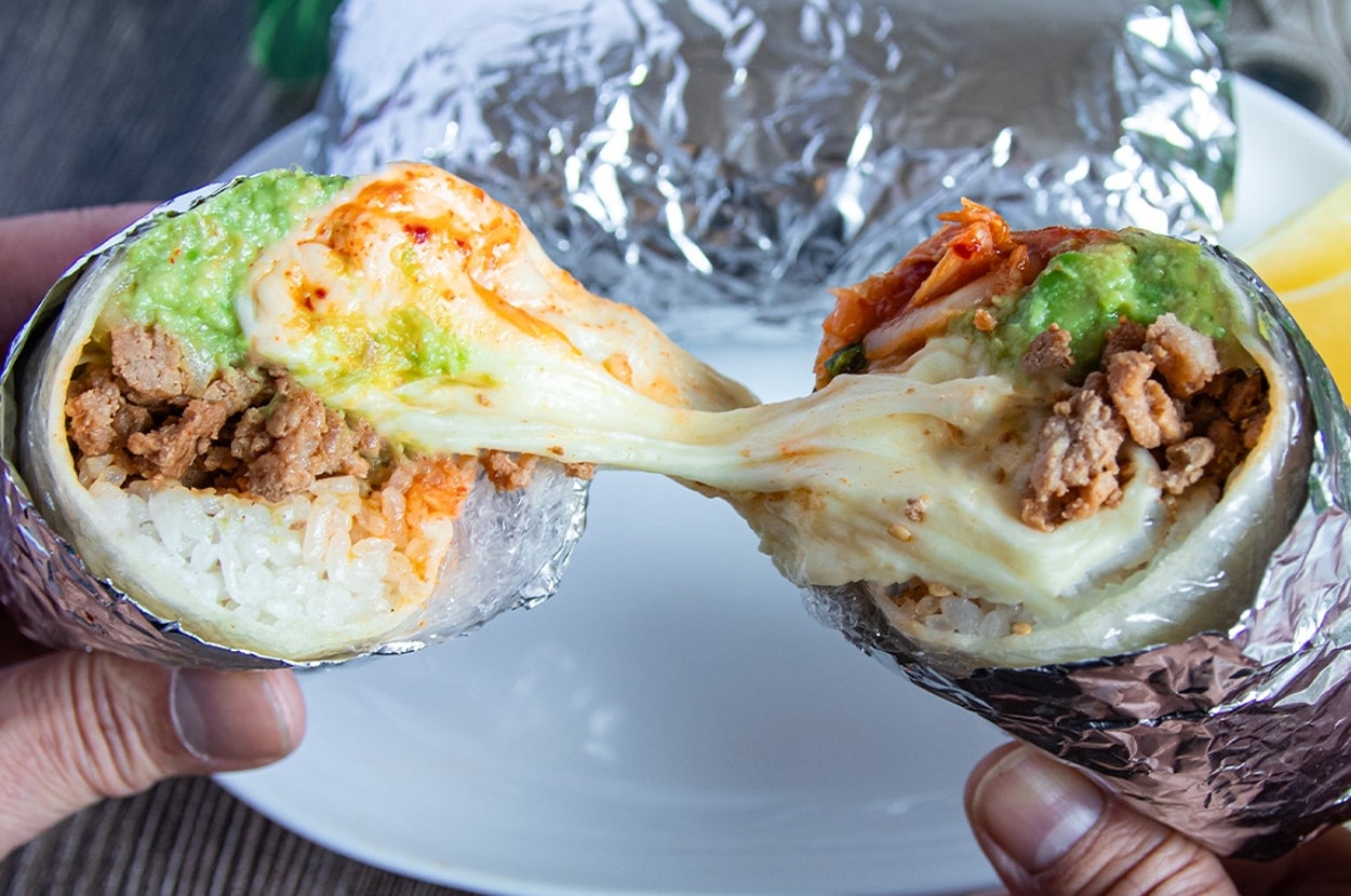 2つのアルミホイルに包まれたブリトーが半分に切られ、中には溶けたチーズ、アボカド、肉、ご飯が見える。