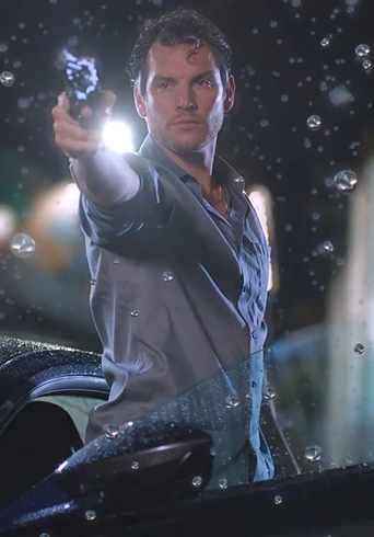 Person aiming a gun, standing by a car in the rain, conveying an intense or dramatic scene