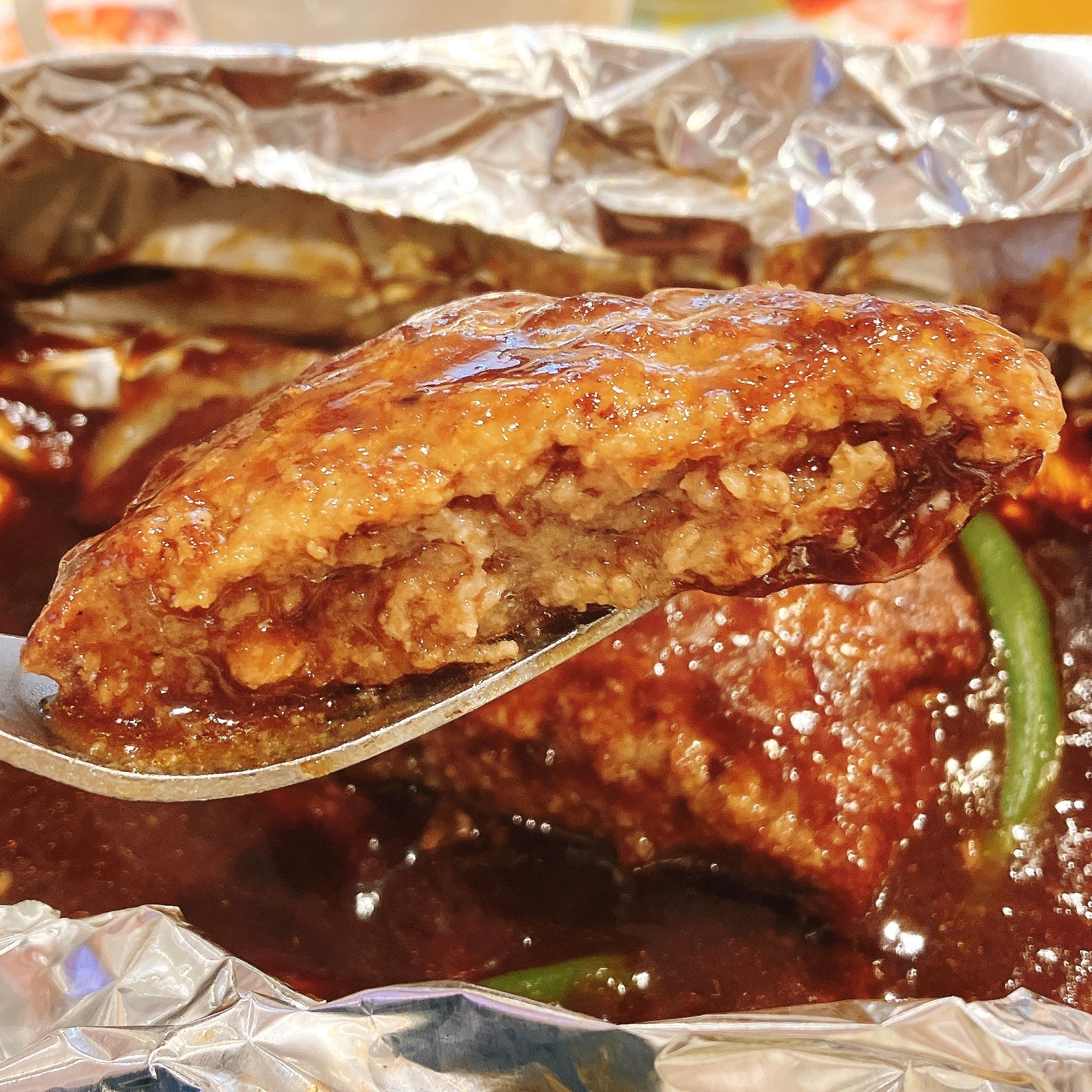 COCO'S（ココス）のモーニング限定メニュー「包み焼きハンバーグの朝定食」アルミホイルに包まれたハンバーグステーキ。スプーンですくわれ、肉汁がしたたっている。
