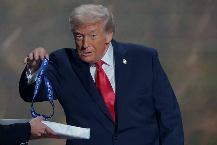 A idiosyncratic   successful  a suit   with a reddish  necktie  holds retired  a lanyard, handing it to idiosyncratic    with a wrapped point  connected  stage