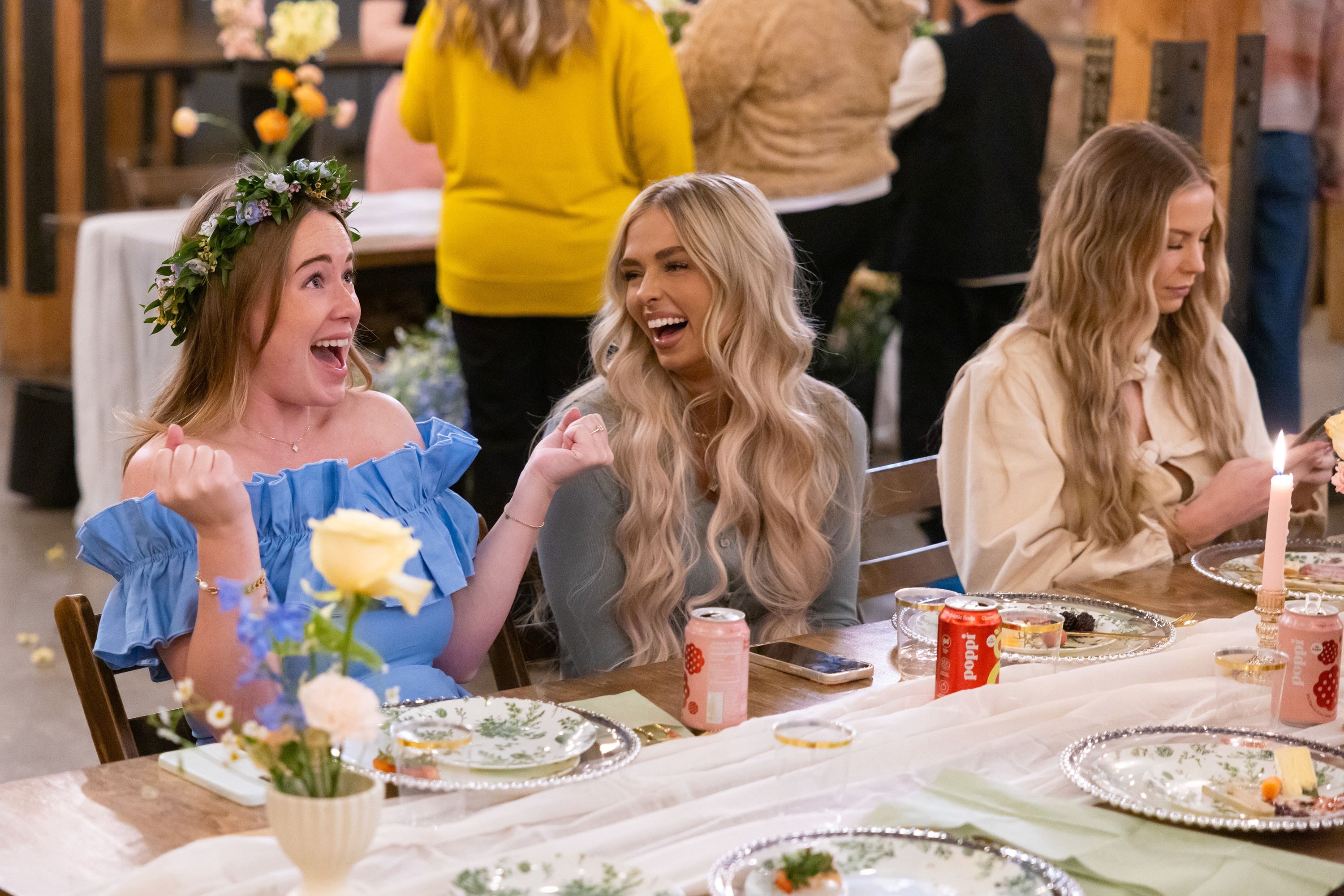 Three women are seated astatine  a eating  table, laughing and enjoying a societal  event. The pistillate   connected  the near  wears a angiosperm  crown