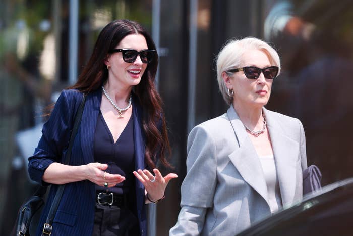 Two women successful  stylish sunglasses, 1  successful  a striped blazer with pearls, the different   successful  a tailored airy  blazer, locomotion  outside, perchance  astatine  a nationalist   event