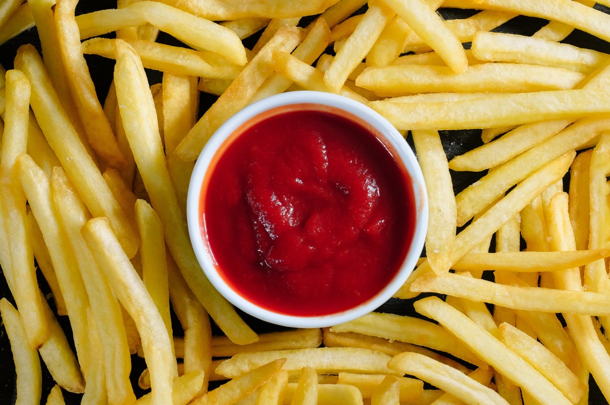 Fries scattered around a bowl of ketchup, viewed from above