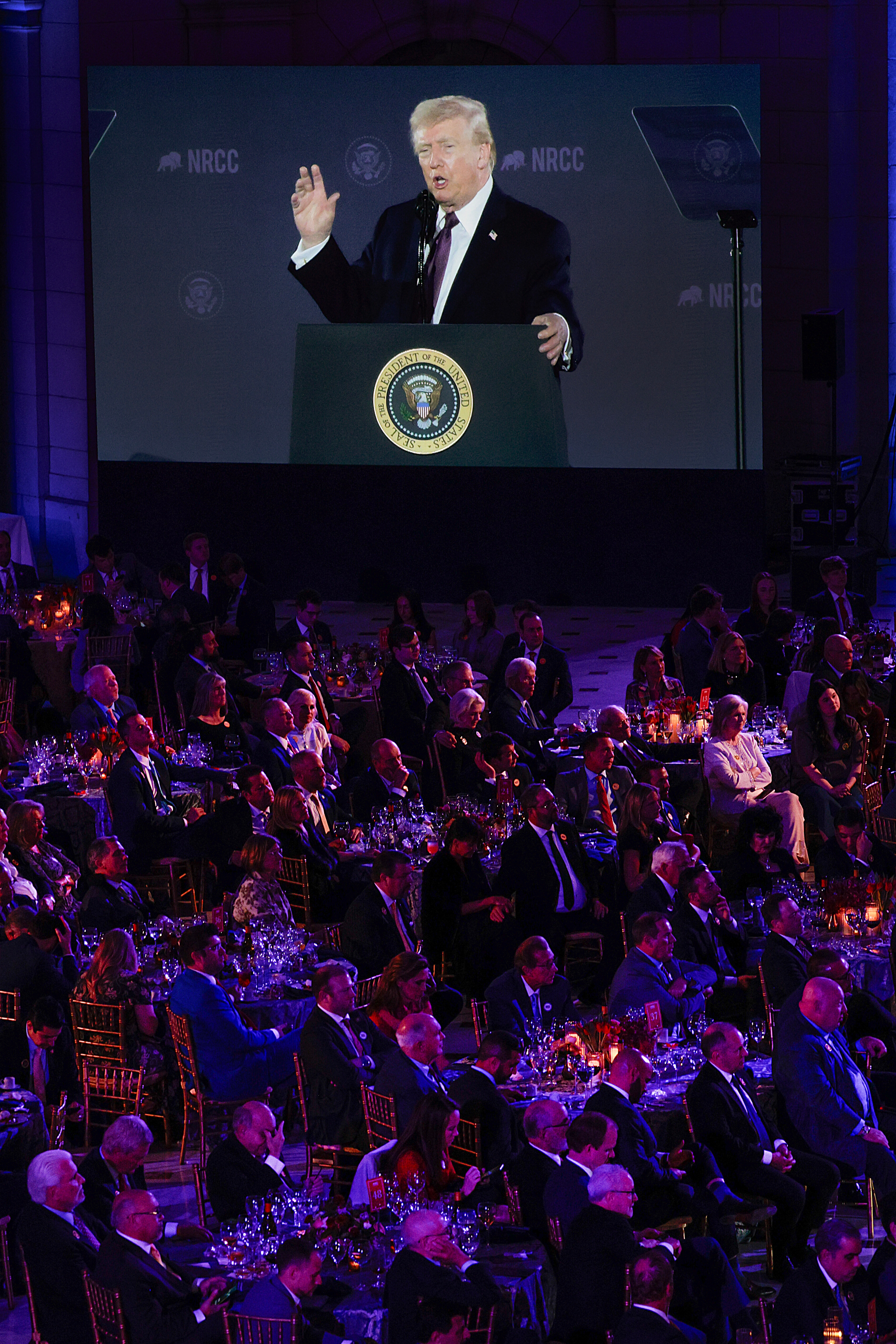 A idiosyncratic speaking astatine a podium during a ceremonial meal event, with a ample assemblage seated astatine tables and the code projected connected a ample screen