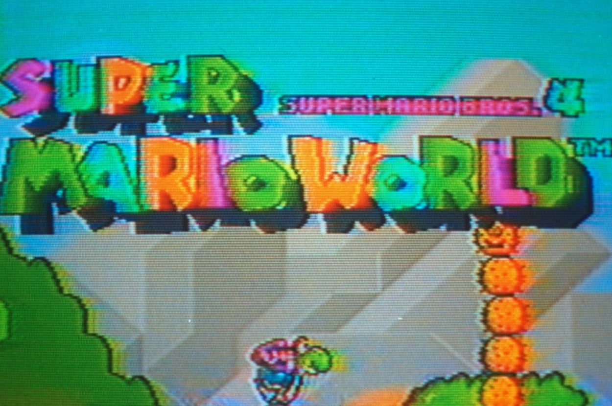 Stylized text "Super Mario World" with Mario riding Yoshi through a level on the game cover