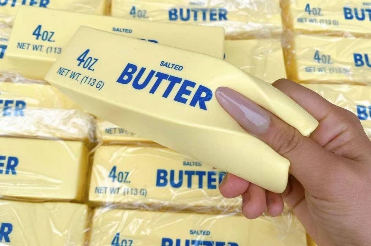 Hand holding a stress toy shaped like a stick of salted butter, with many identical toys in the background