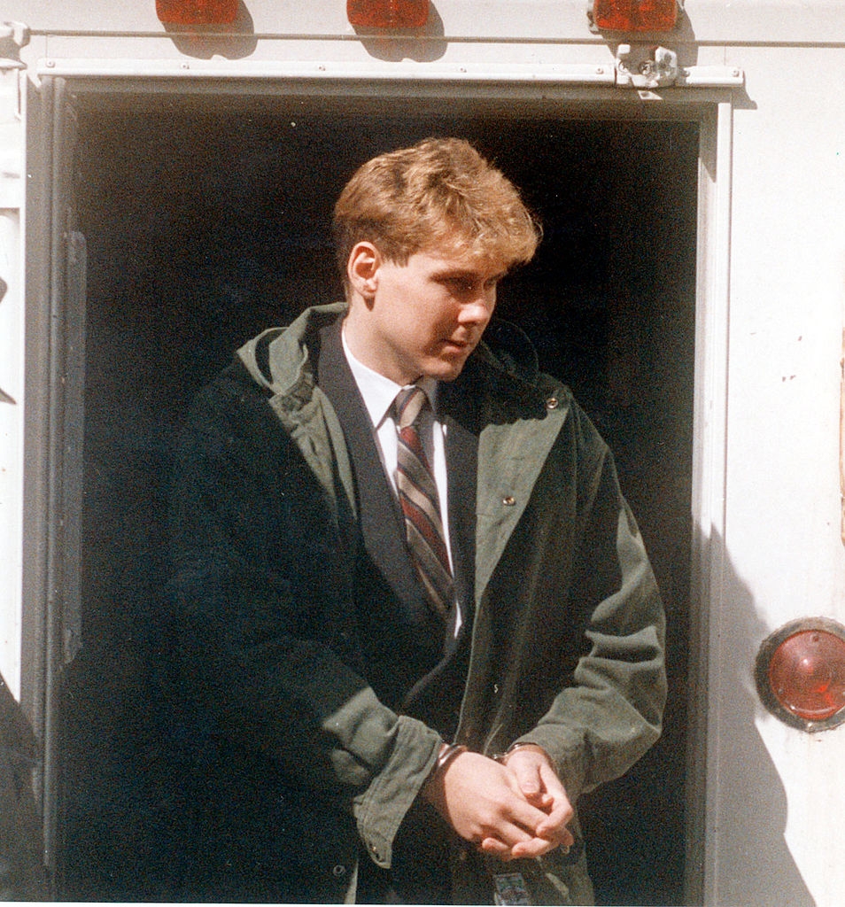 A idiosyncratic successful a suit with a tie, wearing an overcoat, exits a conveyance with hands cuffed