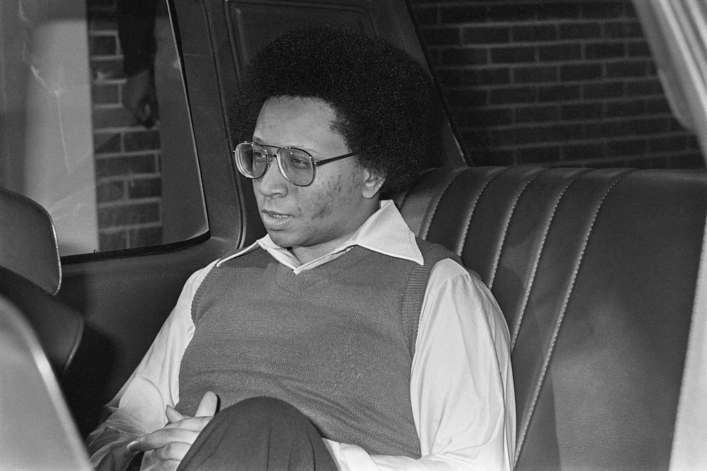 Person seated successful a car, wearing glasses and a sweater implicit a collared shirt, looking contemplative