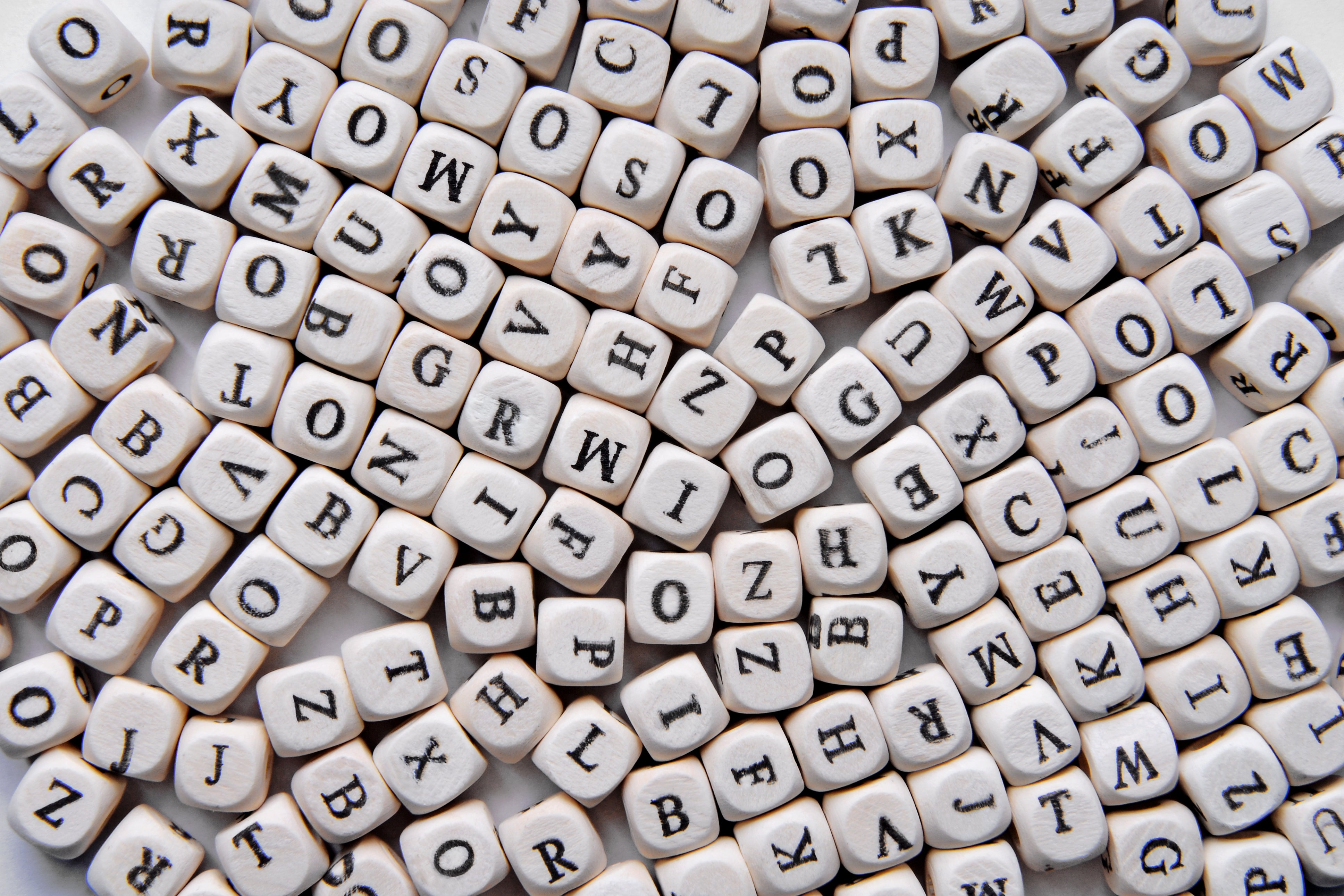 A jumble of lettered dice scattered randomly, illustrating a concept of language or word games