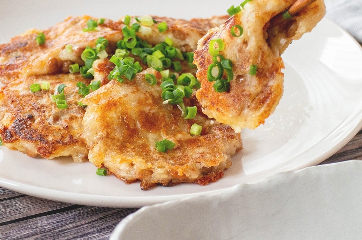 皿に盛られたネギで飾られたお好み焼きを箸で取り分けようとしている。手前にはたれが入った小皿。