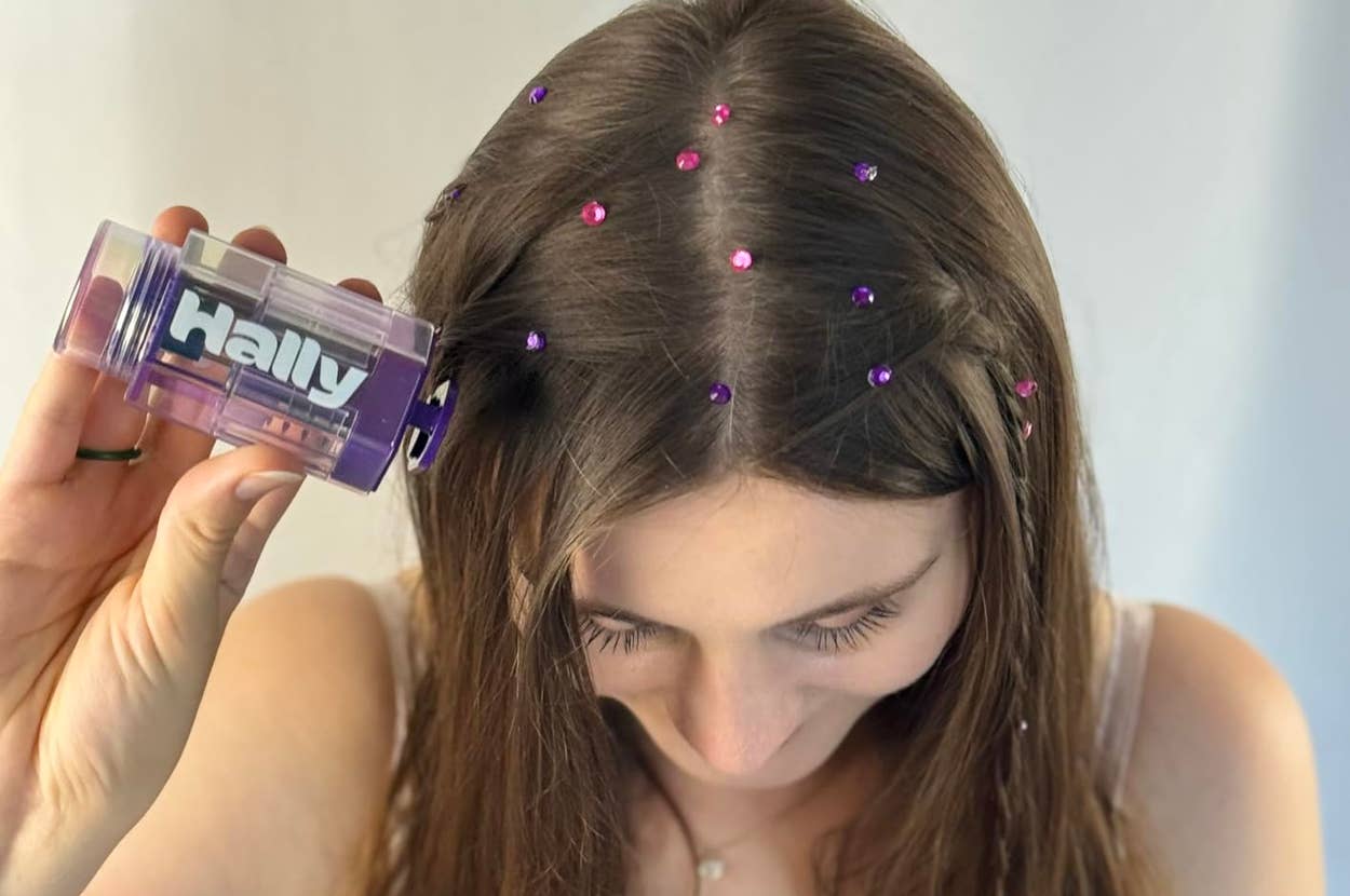 A reviewer with long hair applies colorful hair gems using a small cylindrical tool