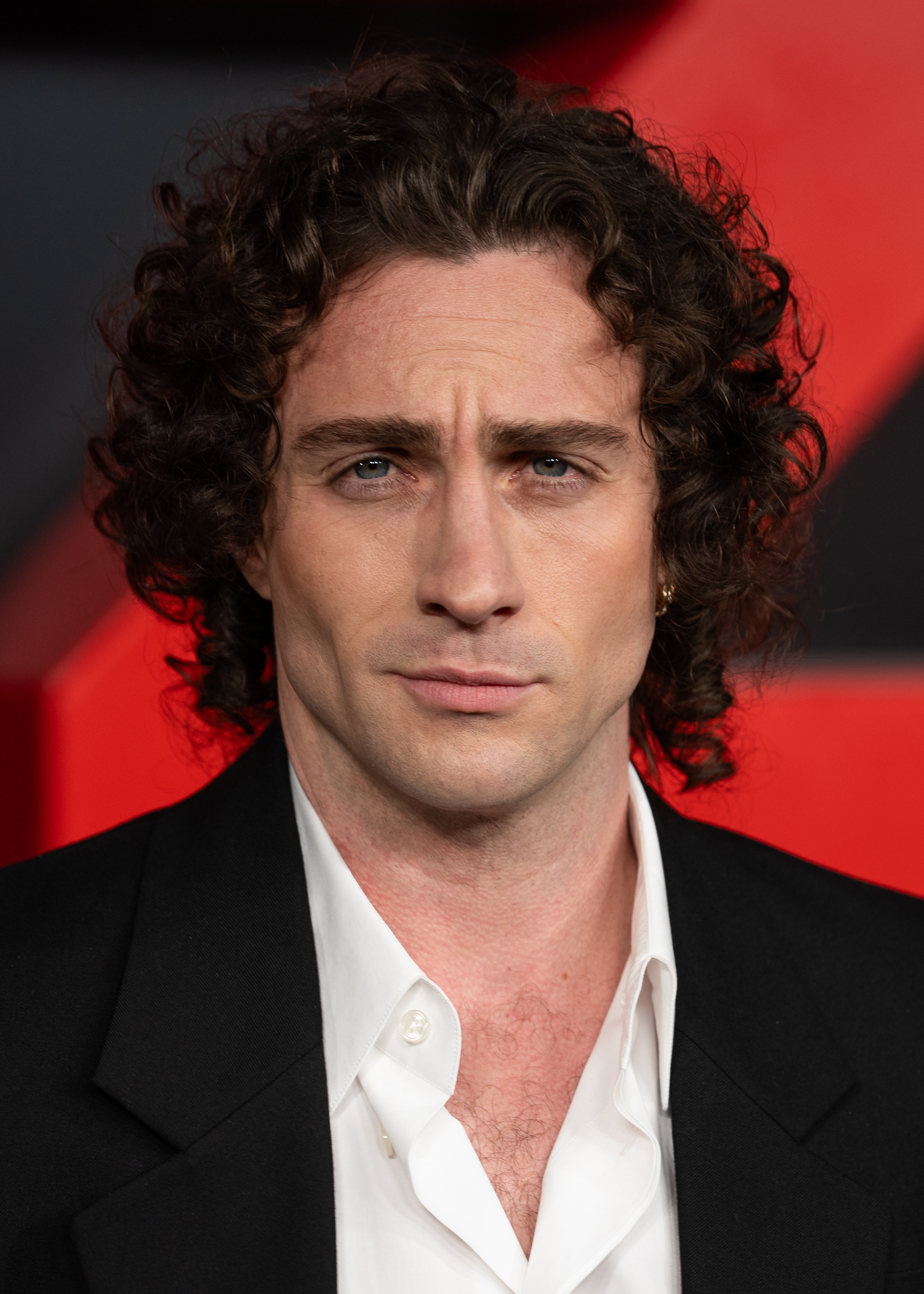 Person with curly hairsbreadth successful a ceremonial suit and achromatic shirt, looking straight astatine the camera