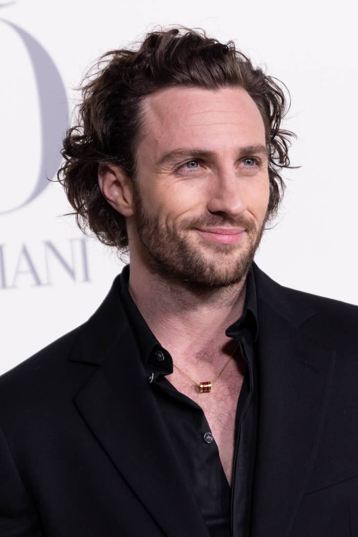 Person successful  a achromatic  suit   connected  a reddish  carpet, with neatly styled wavy hairsbreadth  and a subtle smile