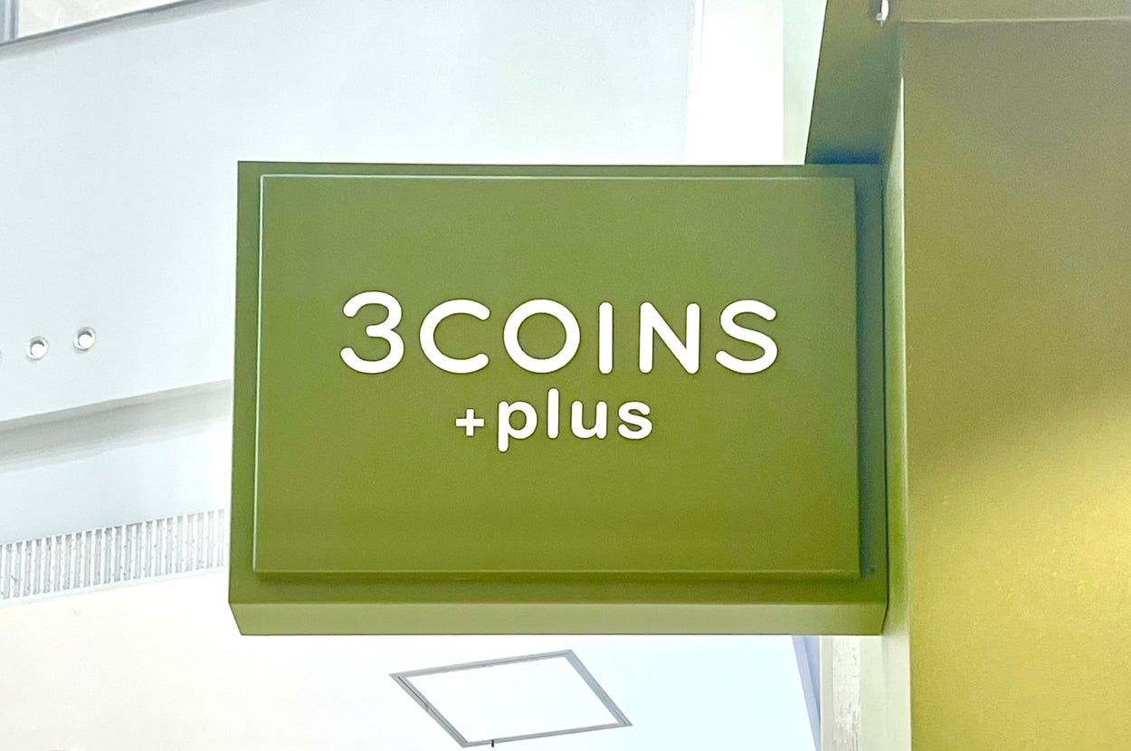 緑の背景に「3COINS +plus」と書かれた店舗の看板。