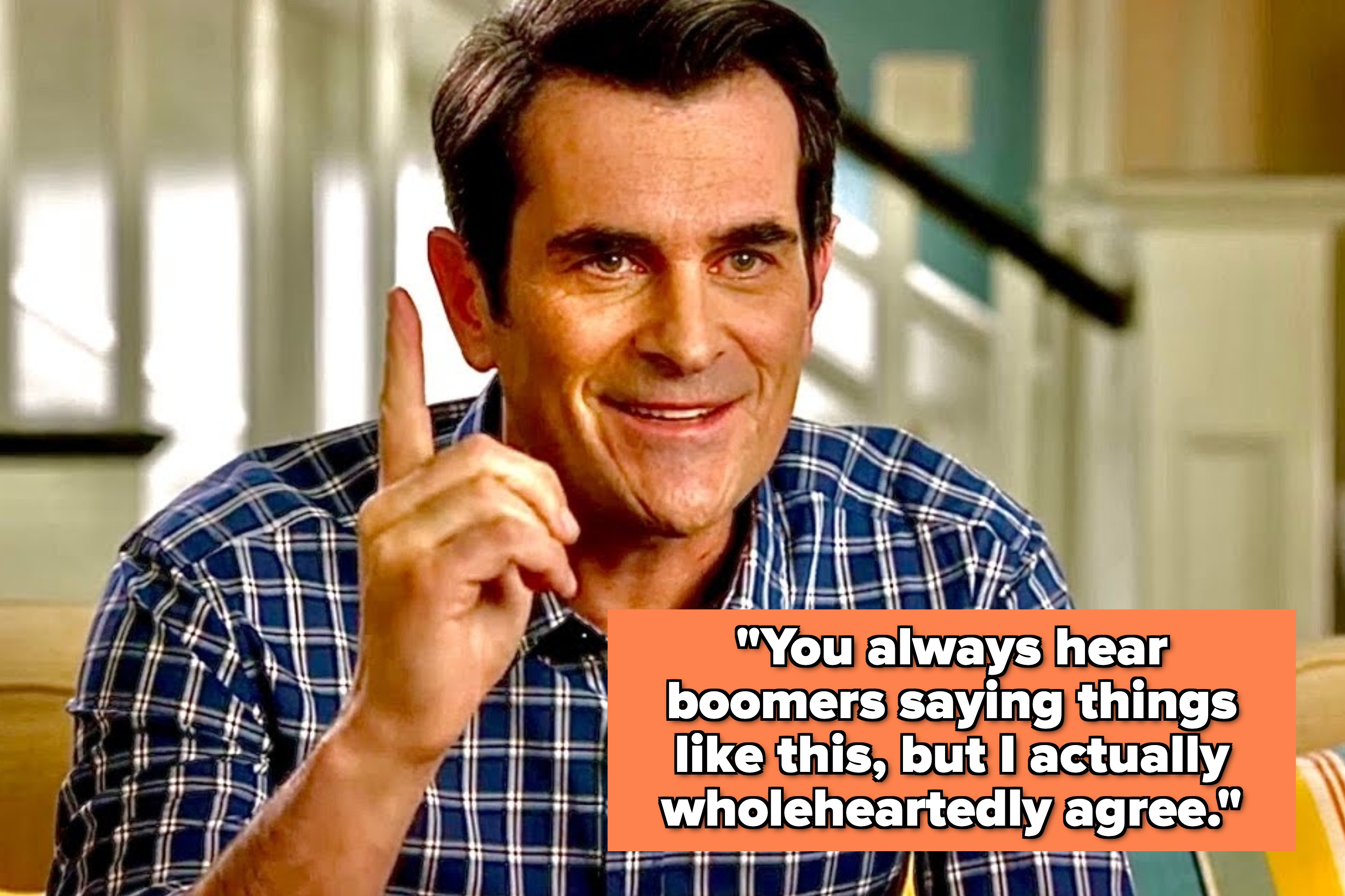 Person in a checkered shirt smiles and raises one finger, appearing to emphasize a point in a casual home setting