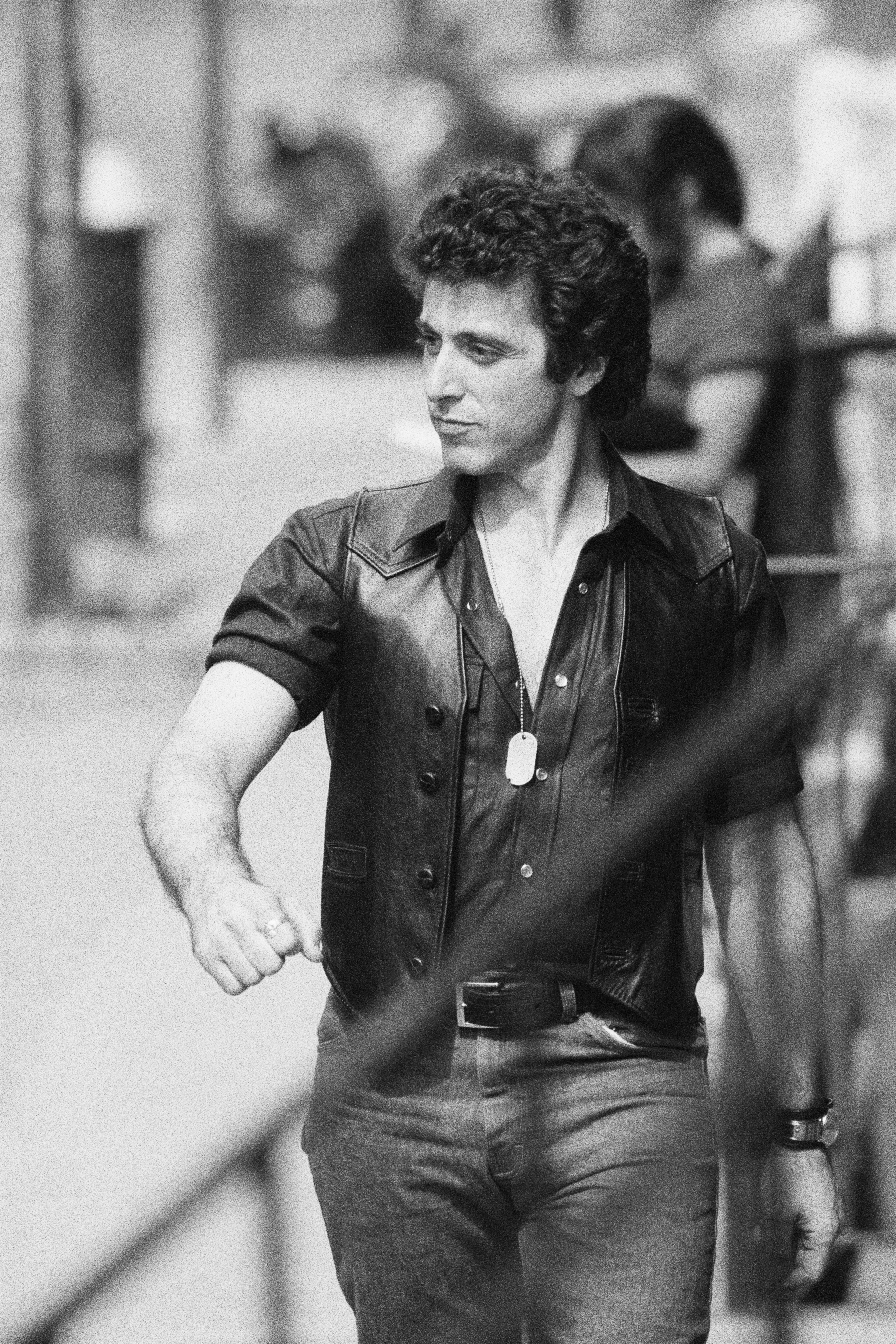 Person wearing a leather vest implicit    a button-up garment  and jeans walks down   a street