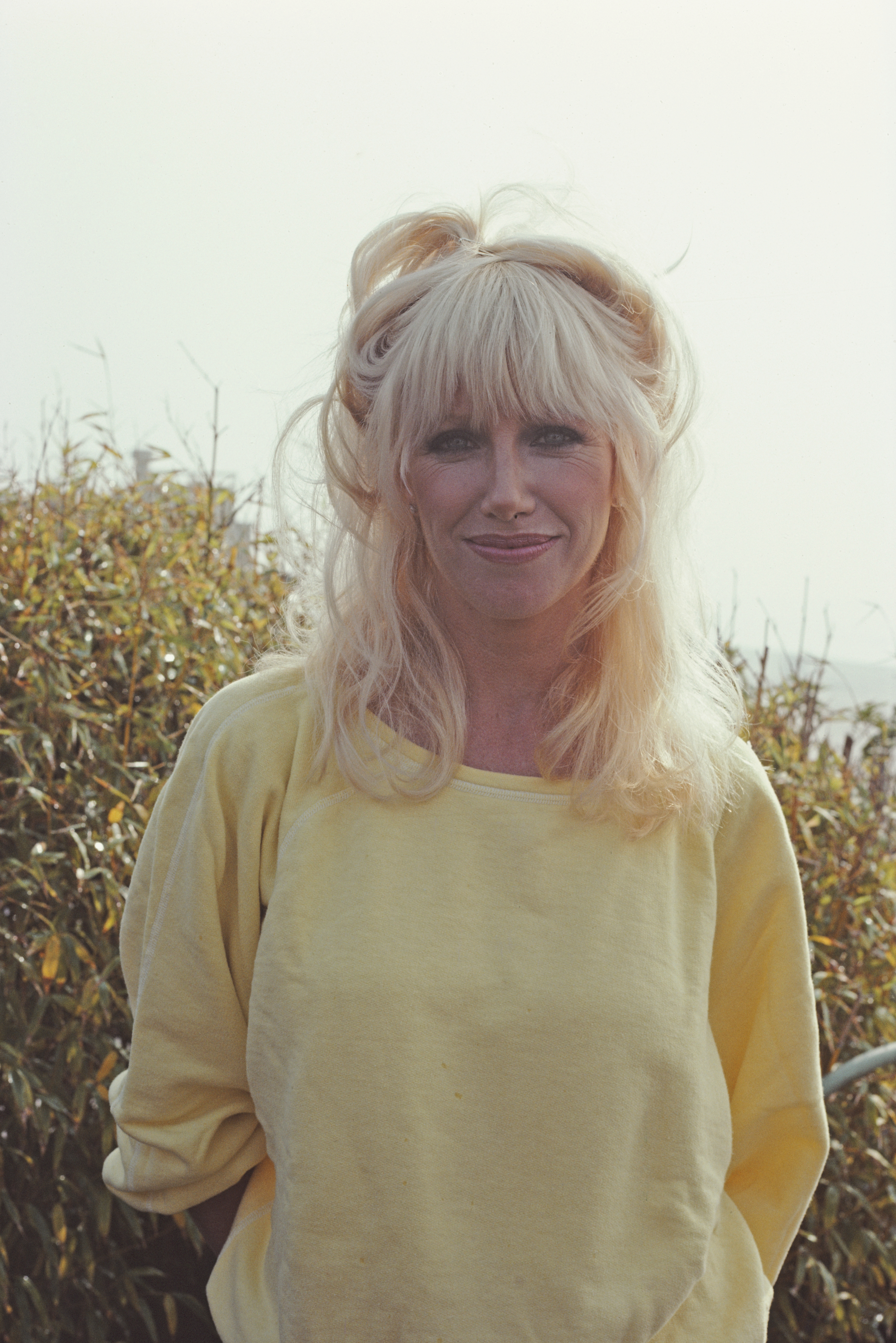 Person with wavy blond hairsbreadth  wearing a casual yellowish  top, lasting  extracurricular  adjacent   foliage