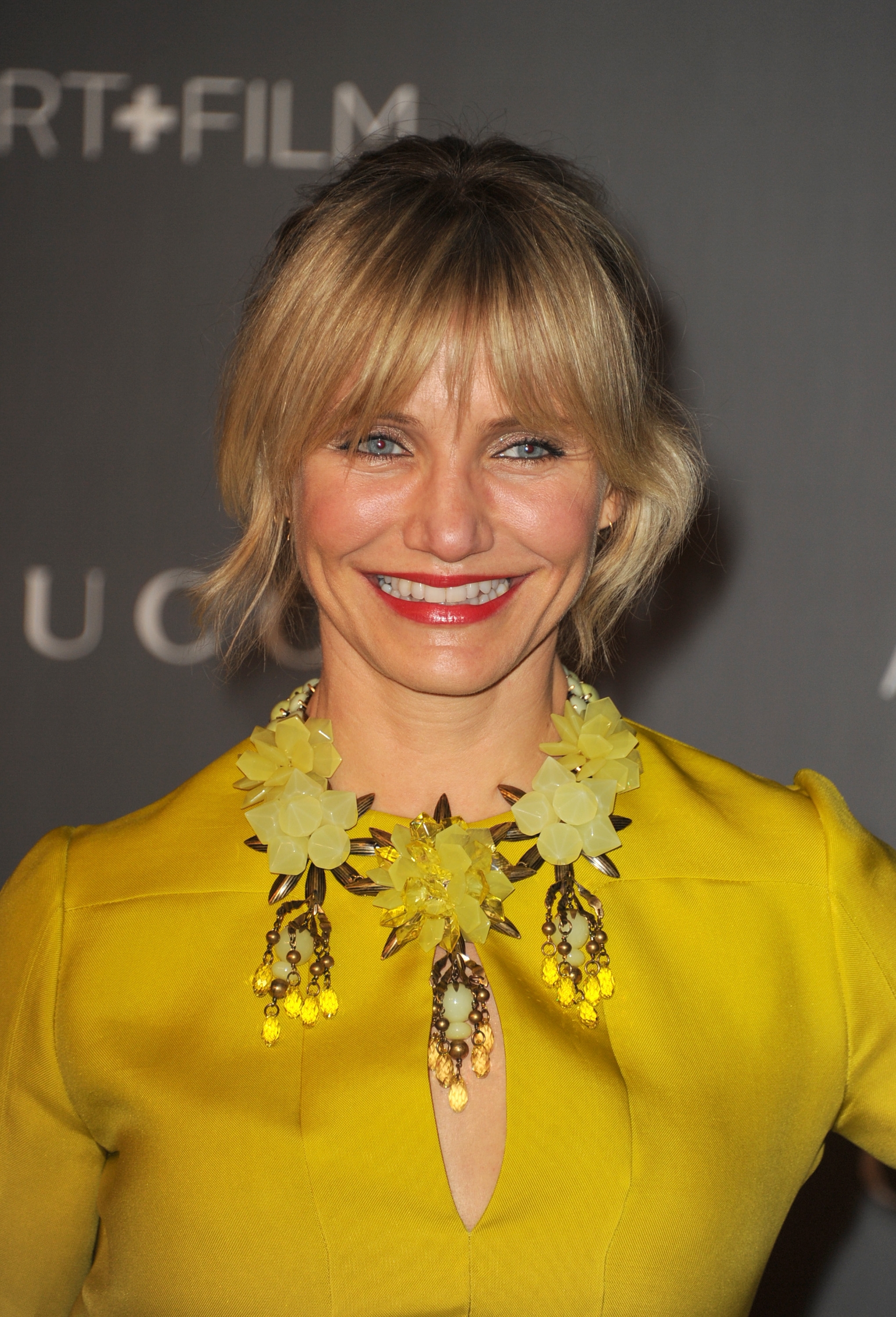 Person smiling connected  a reddish  carpet, wearing a connection    necklace and a stylish apical  with a precocious   neckline