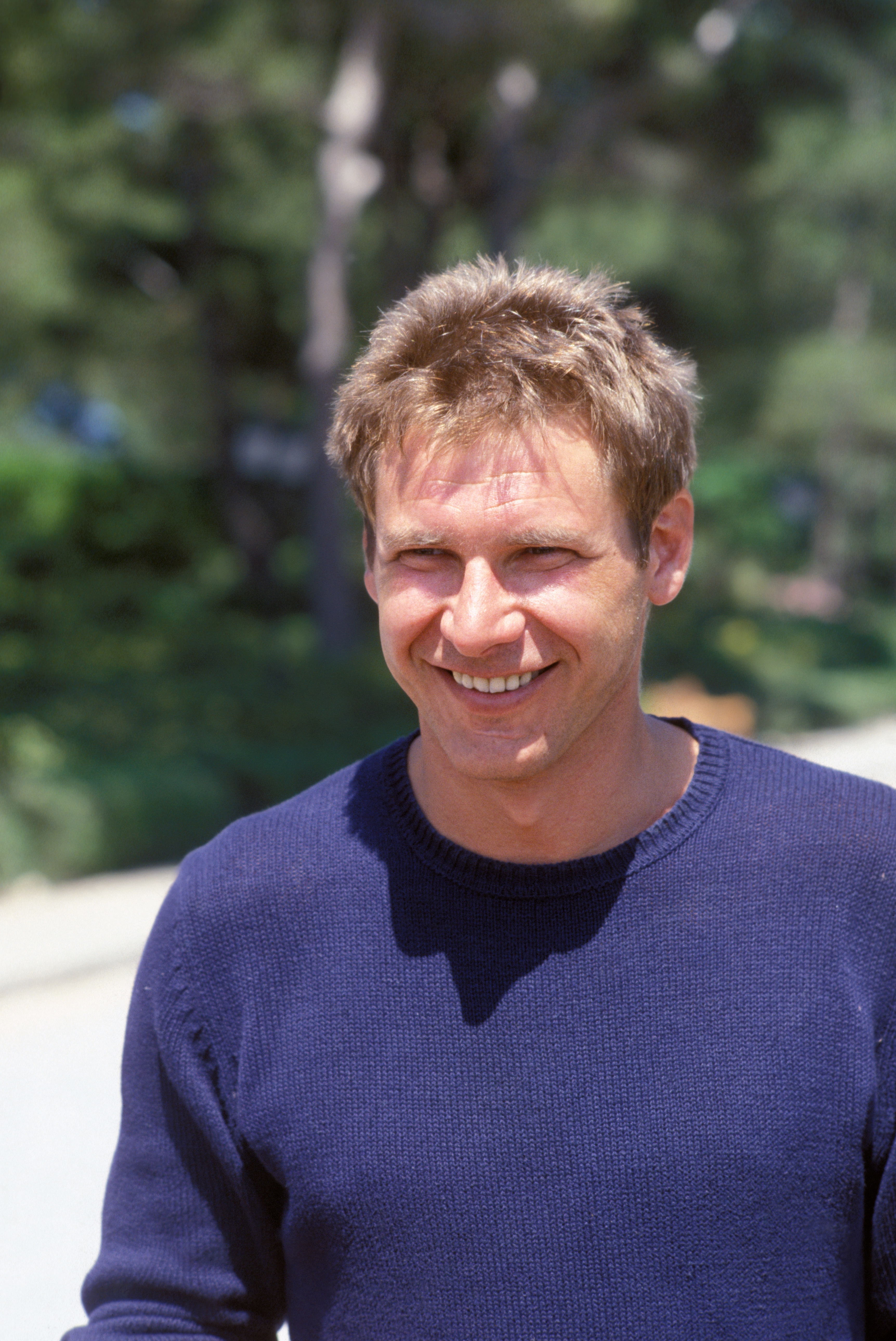 Person outdoors, smiling, wearing a casual sweater with abbreviated  hair