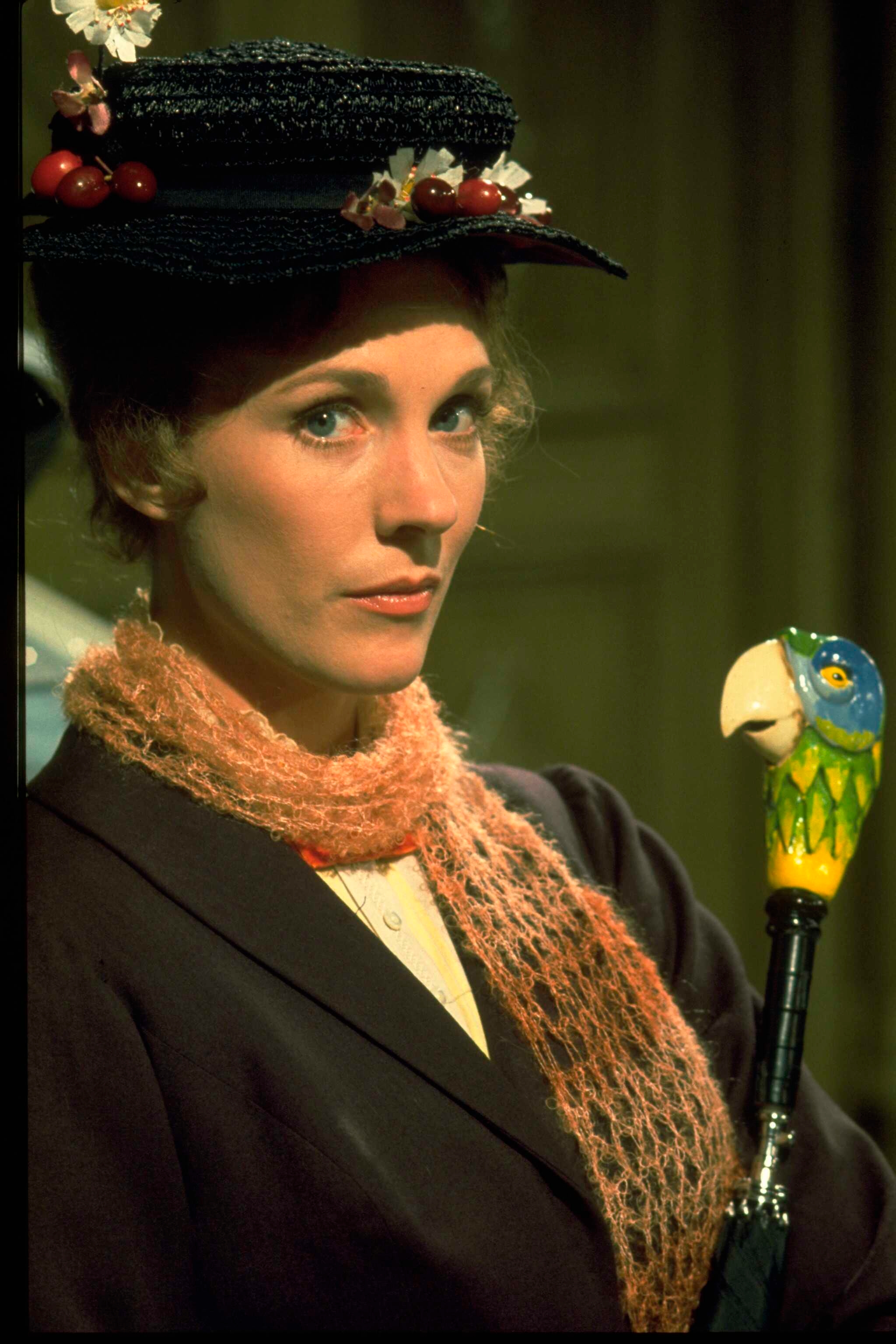 Person dressed successful  vintage-style clothing, wearing a chapeau  adorned with flowers, holding a parrot-handled umbrella