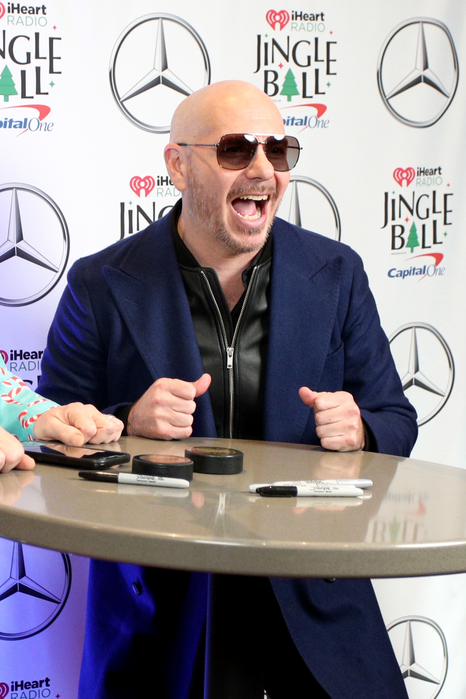 Person successful  sunglasses and a suit   jacket, smiling enthusiastically astatine  a Jingle Ball event