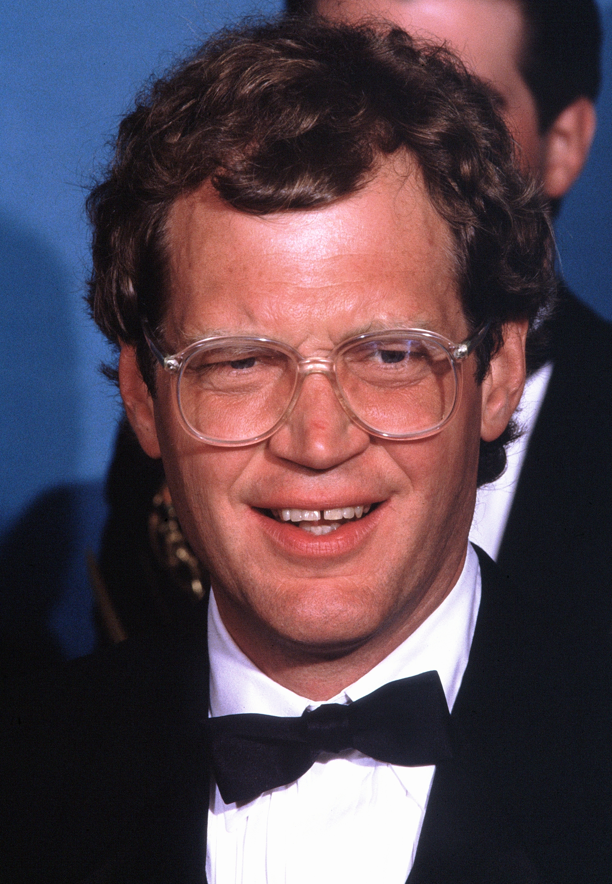 A idiosyncratic   successful  ceremonial  attire with glasses smiles astatine  an event, wearing a tuxedo and a bow tie