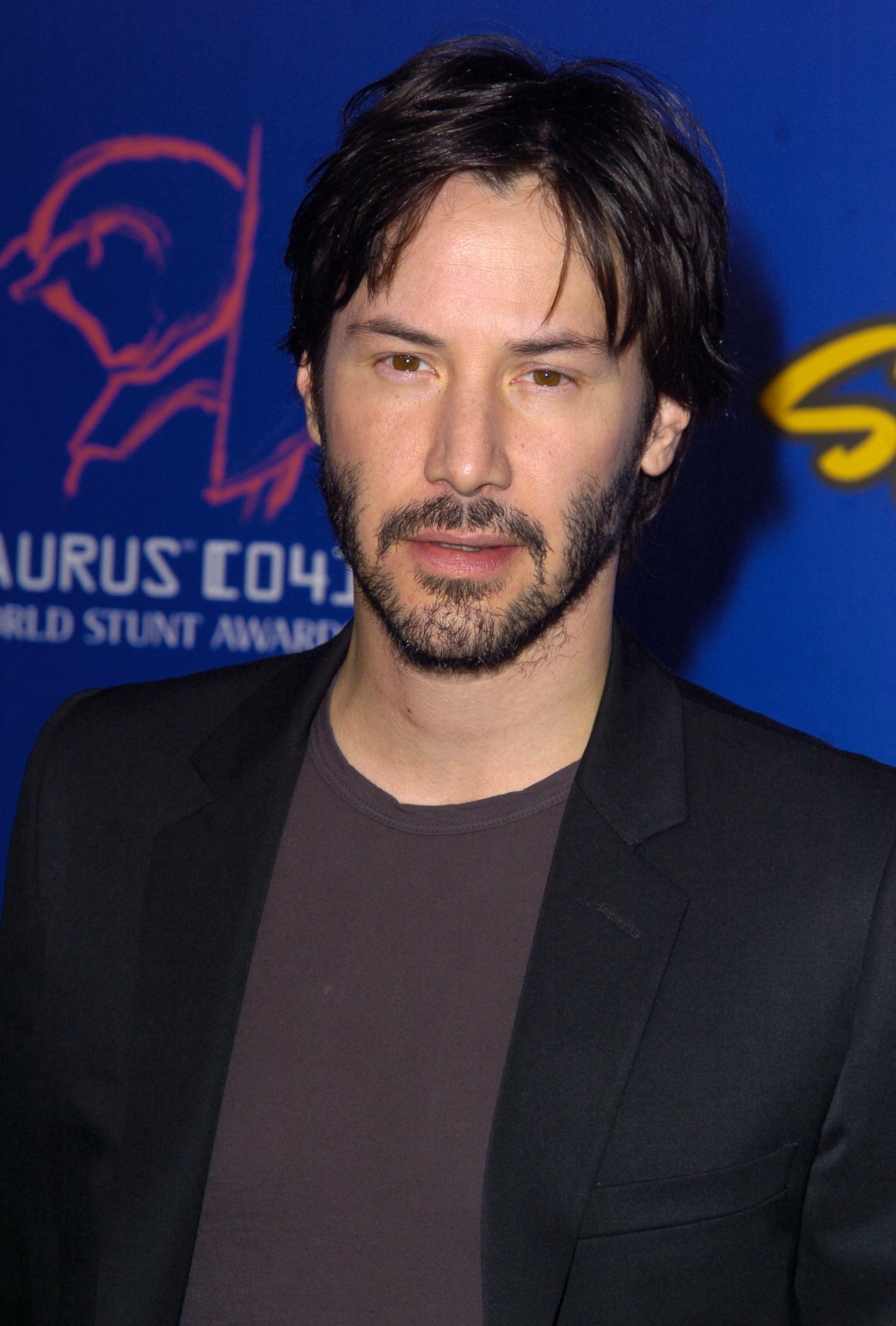 A idiosyncratic   successful  a suit   and t-shirt attends an event. The inheritance  features a logo and the words "World Stunt Awards."