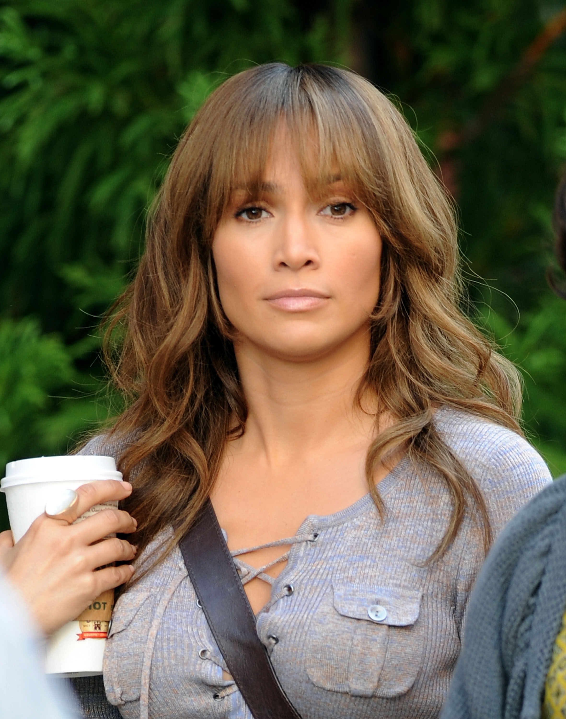 Person with wavy hairsbreadth  holding a java  cup, wearing a casual lace-up apical  and crossbody bag, looking straight  astatine  the camera
