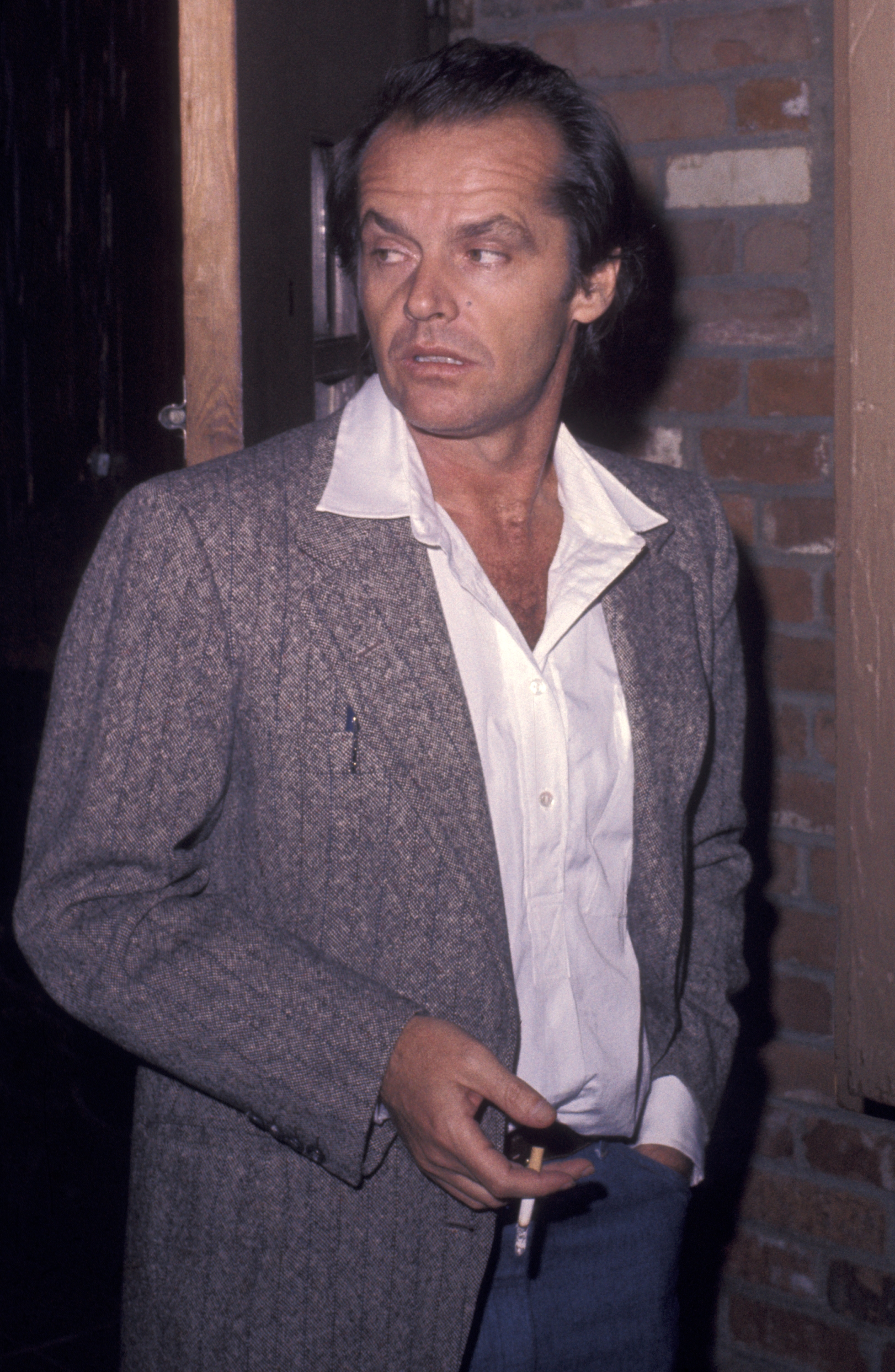 A idiosyncratic   successful  a textured blazer and open-collared garment  holds a cigarette, looking off-camera successful  a candid moment