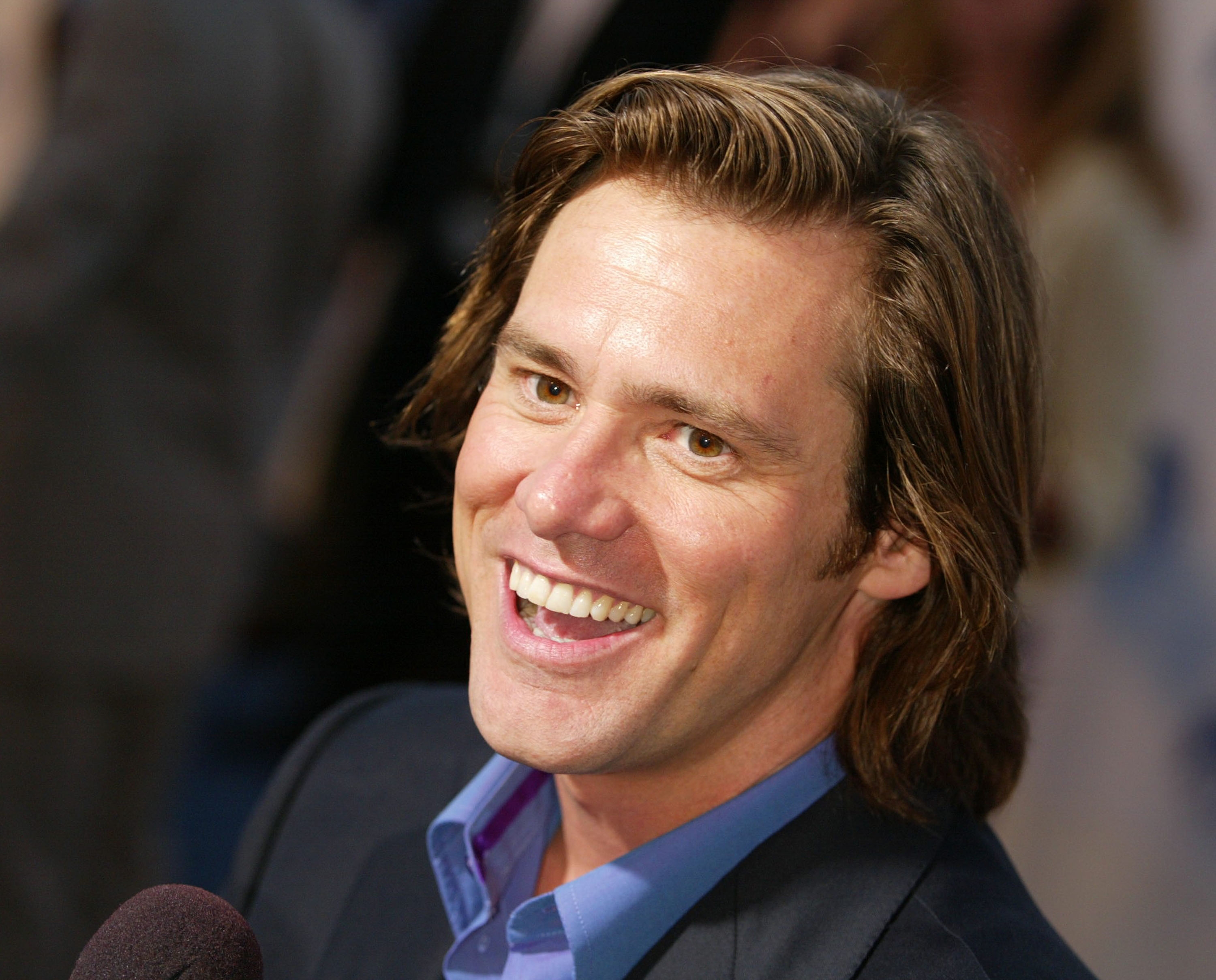 Smiling idiosyncratic   connected  a reddish  carpet, wearing a acheronian  suit   and bluish  shirt, speaking into a microphone