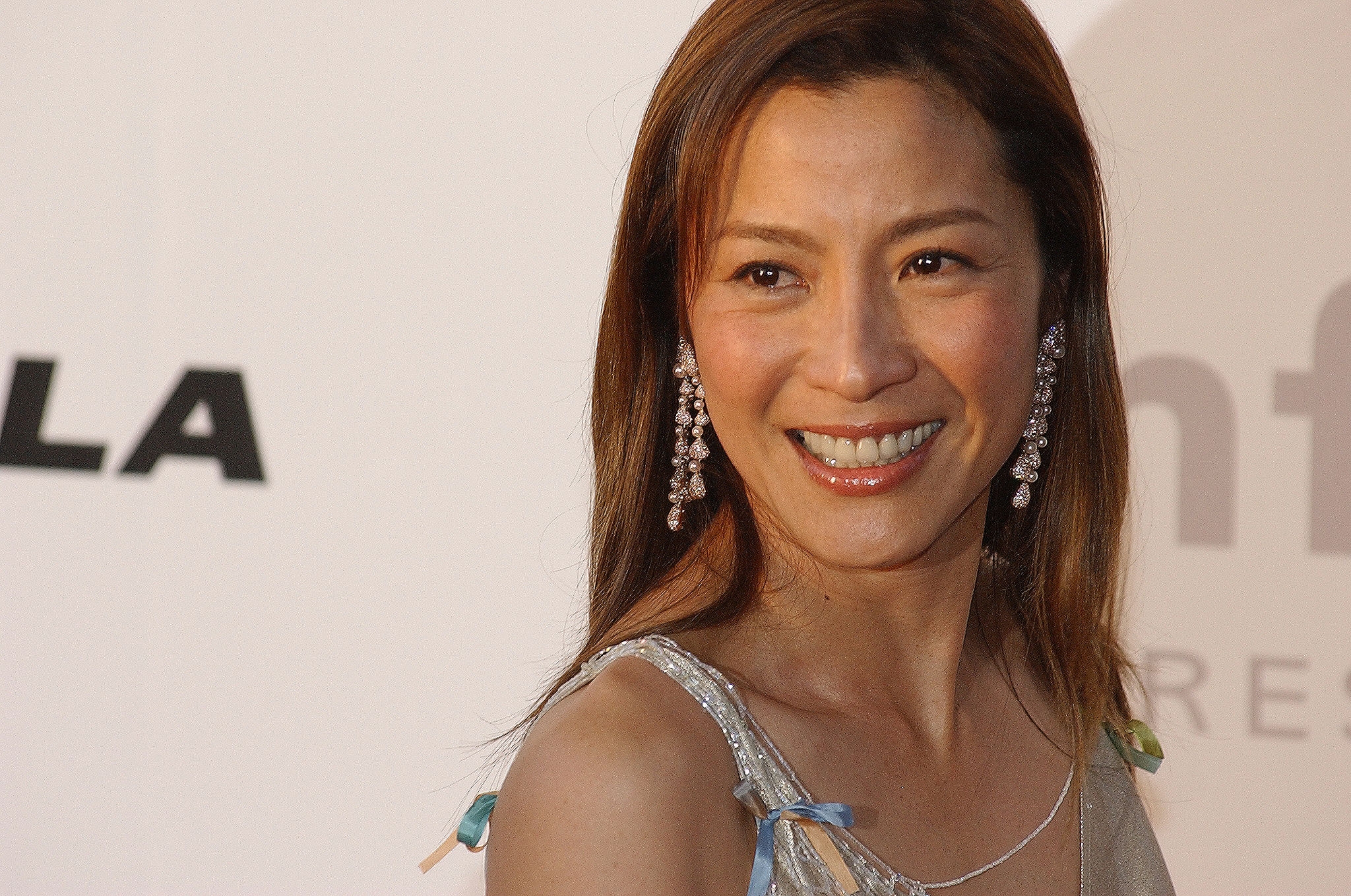 Woman connected  reddish  carpet smiling, wearing connection    earrings and a sleeveless embellished gown