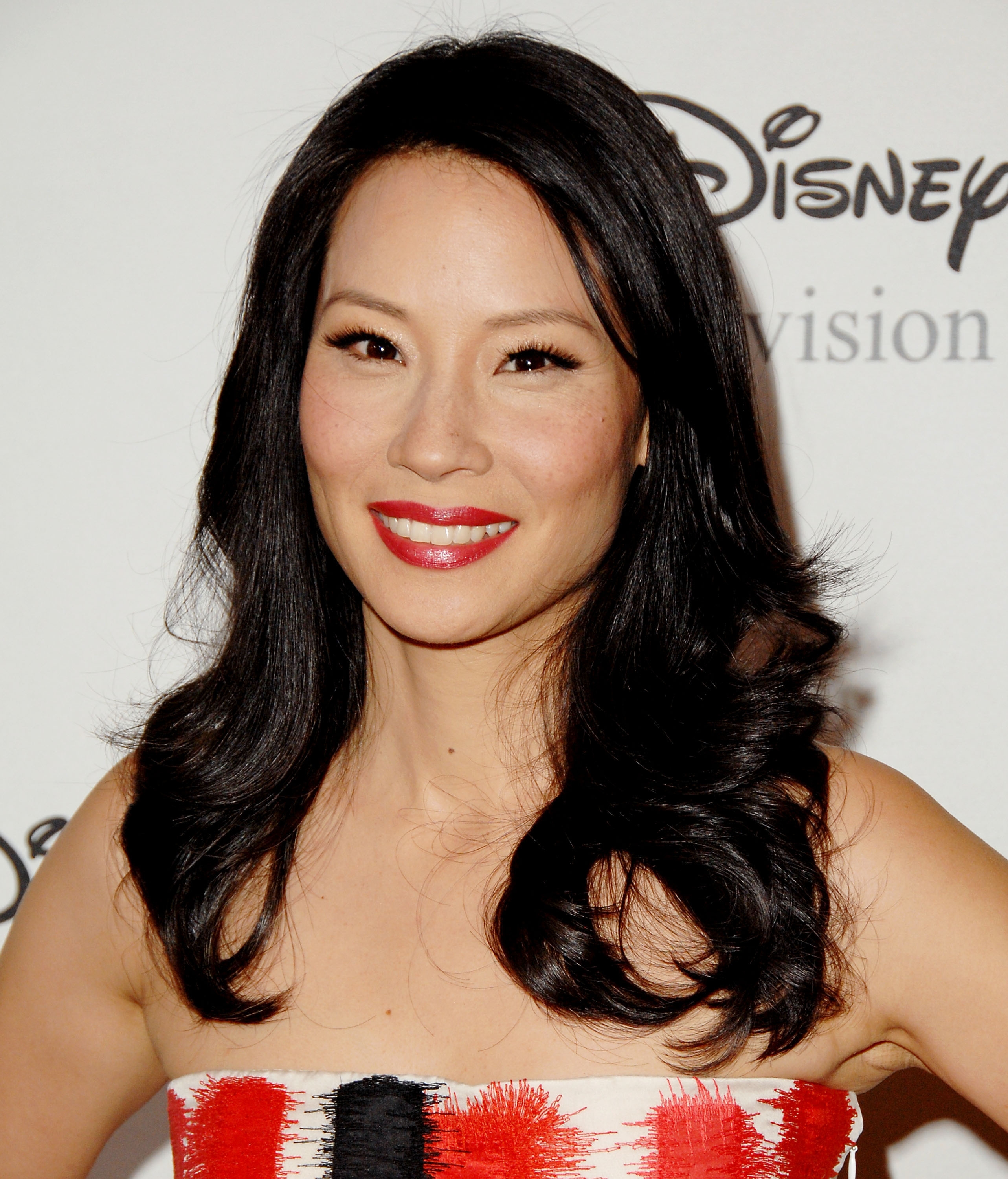 A idiosyncratic   successful  a strapless formal  with a patterned plan  poses astatine  an lawsuit   with a Disney Television backdrop