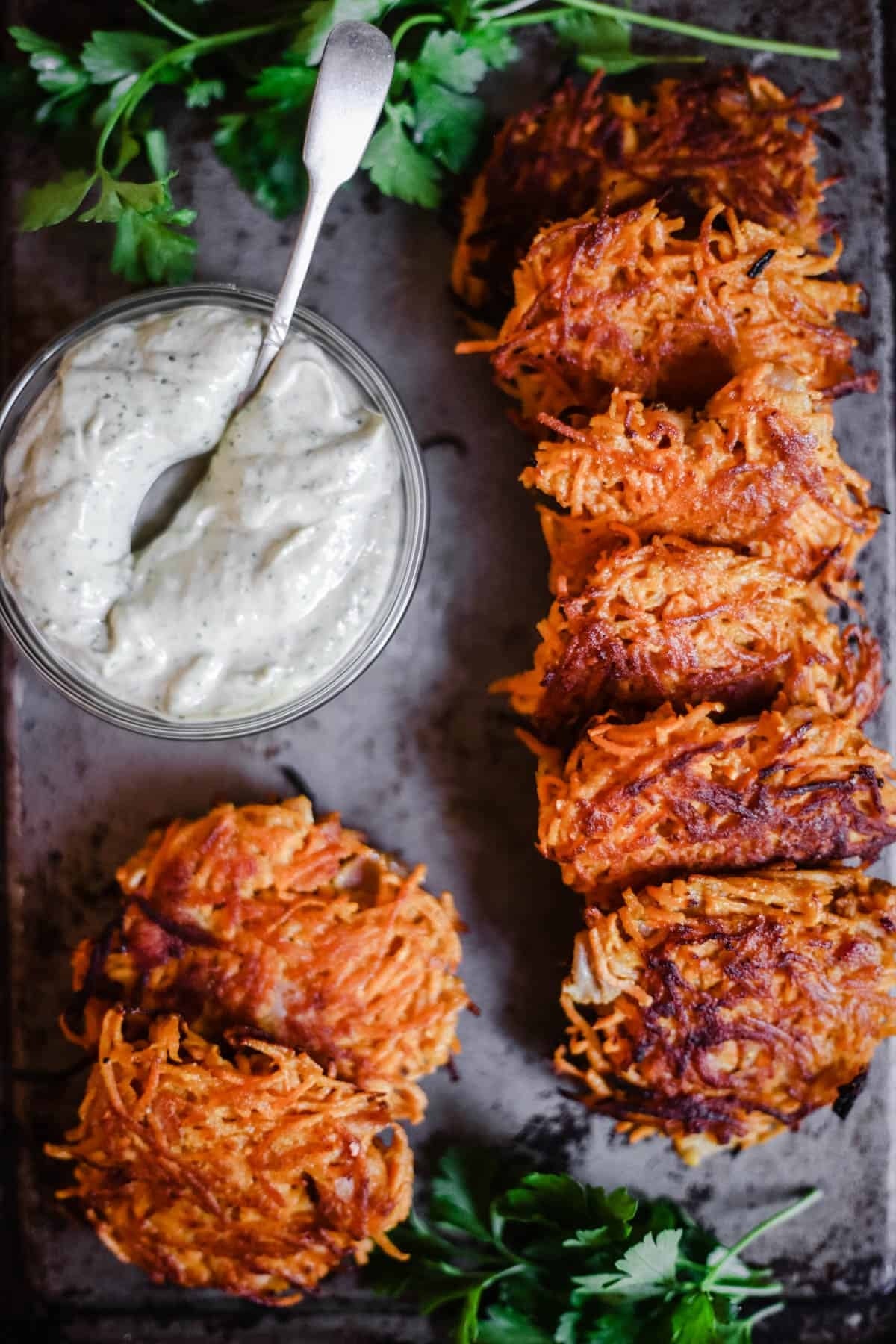 Crispy potato fritters with a bowl of creamy dipping sauce, garnished with fresh herbs