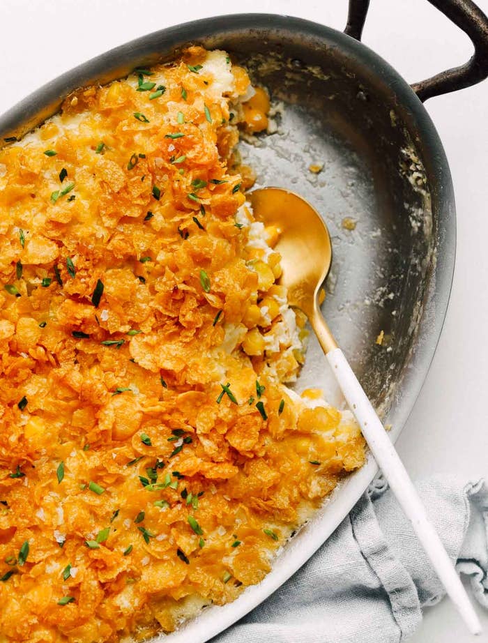 Casserole dish with a baked cornflake topping and a serving spoon in it, resting on a cloth napkin