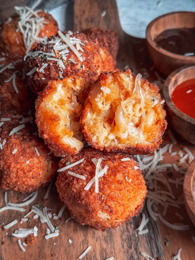 Fried cheese balls garnished with shredded cheese on a wooden board, accompanied by dipping sauces