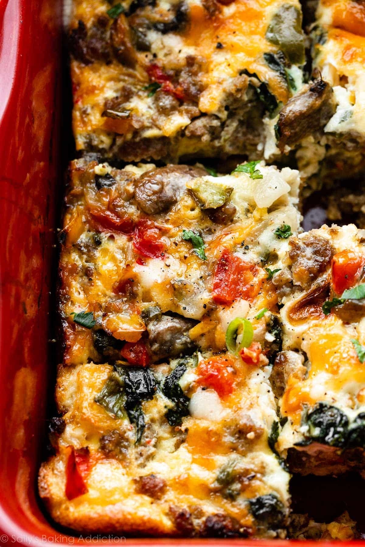 Close-up of a baked breakfast casserole with visible chunks of vegetables, sausage, and melted cheese in a baking dish