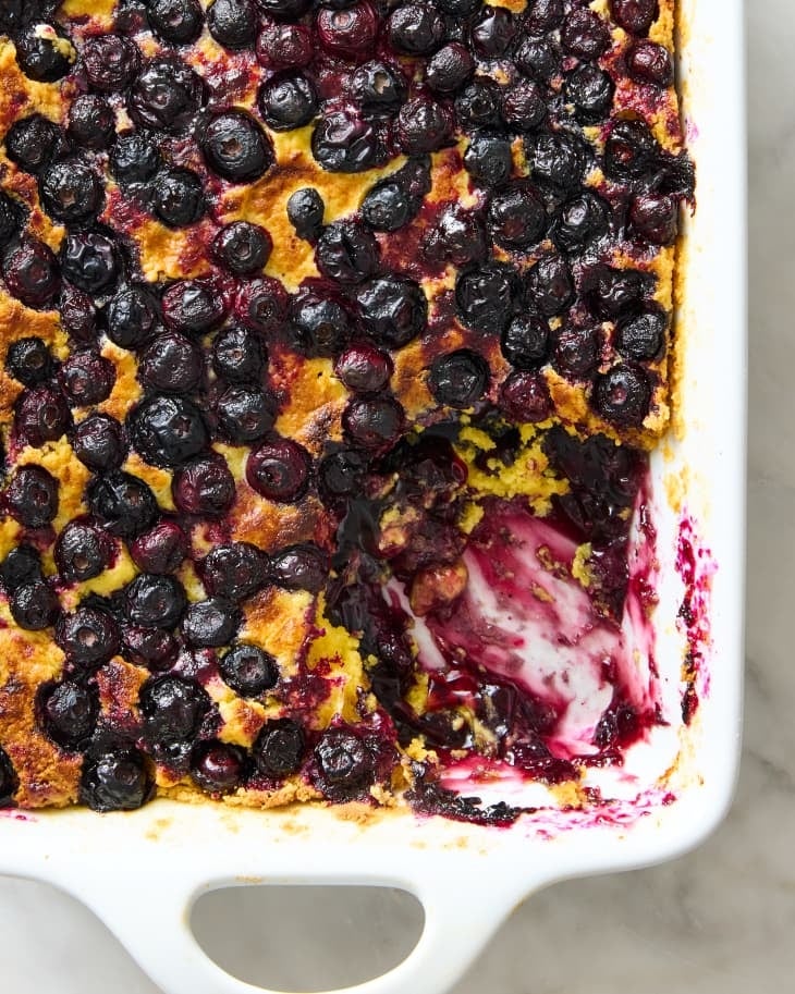 Baked blueberry French toast casserole with a portion missing, showing creamy layers beneath the blueberries