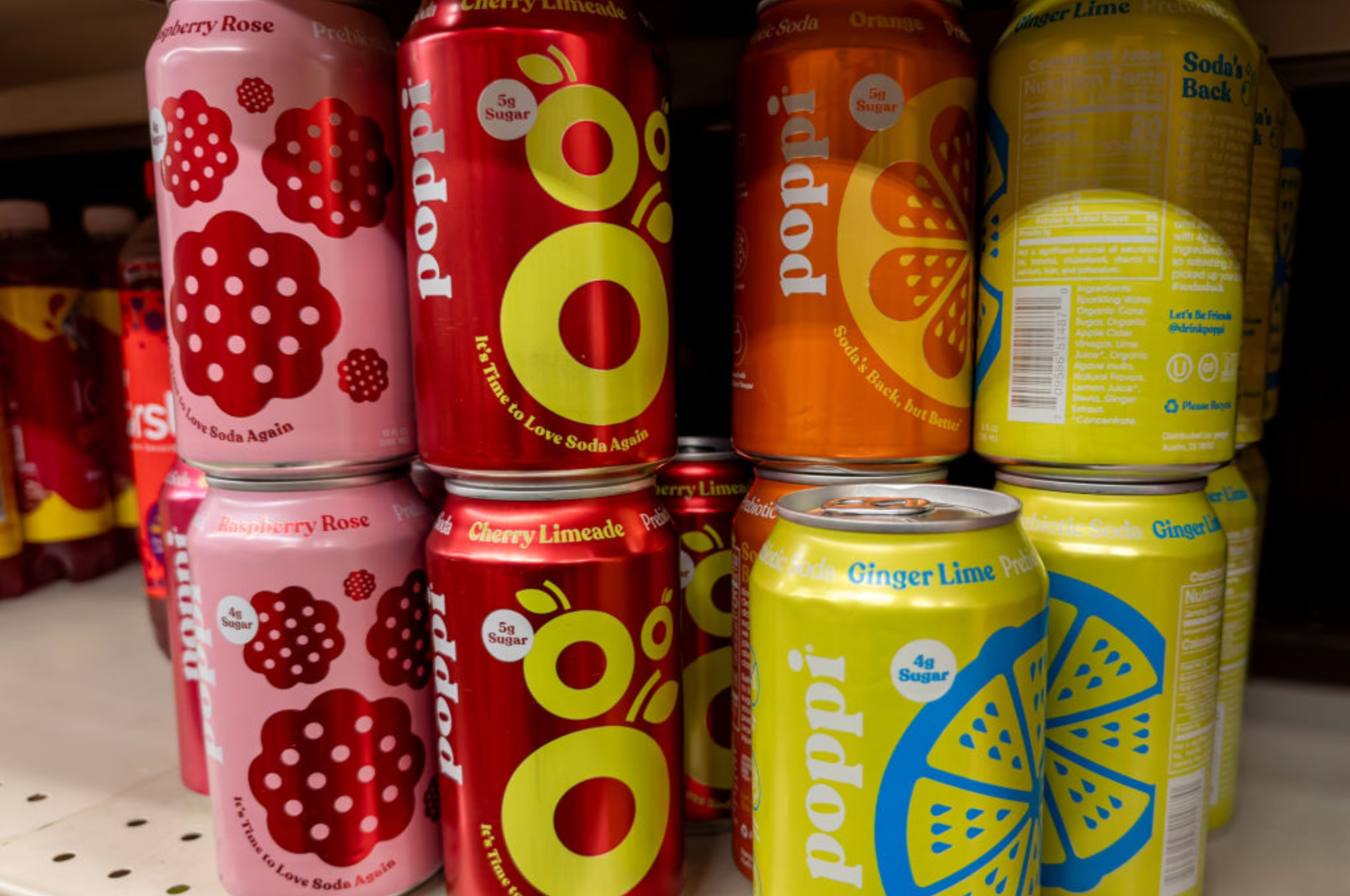 Cans of Poppi soda in various flavors, including Raspberry Rose, Cherry Limeade, Orange, and Ginger Lime, displayed on a store shelf