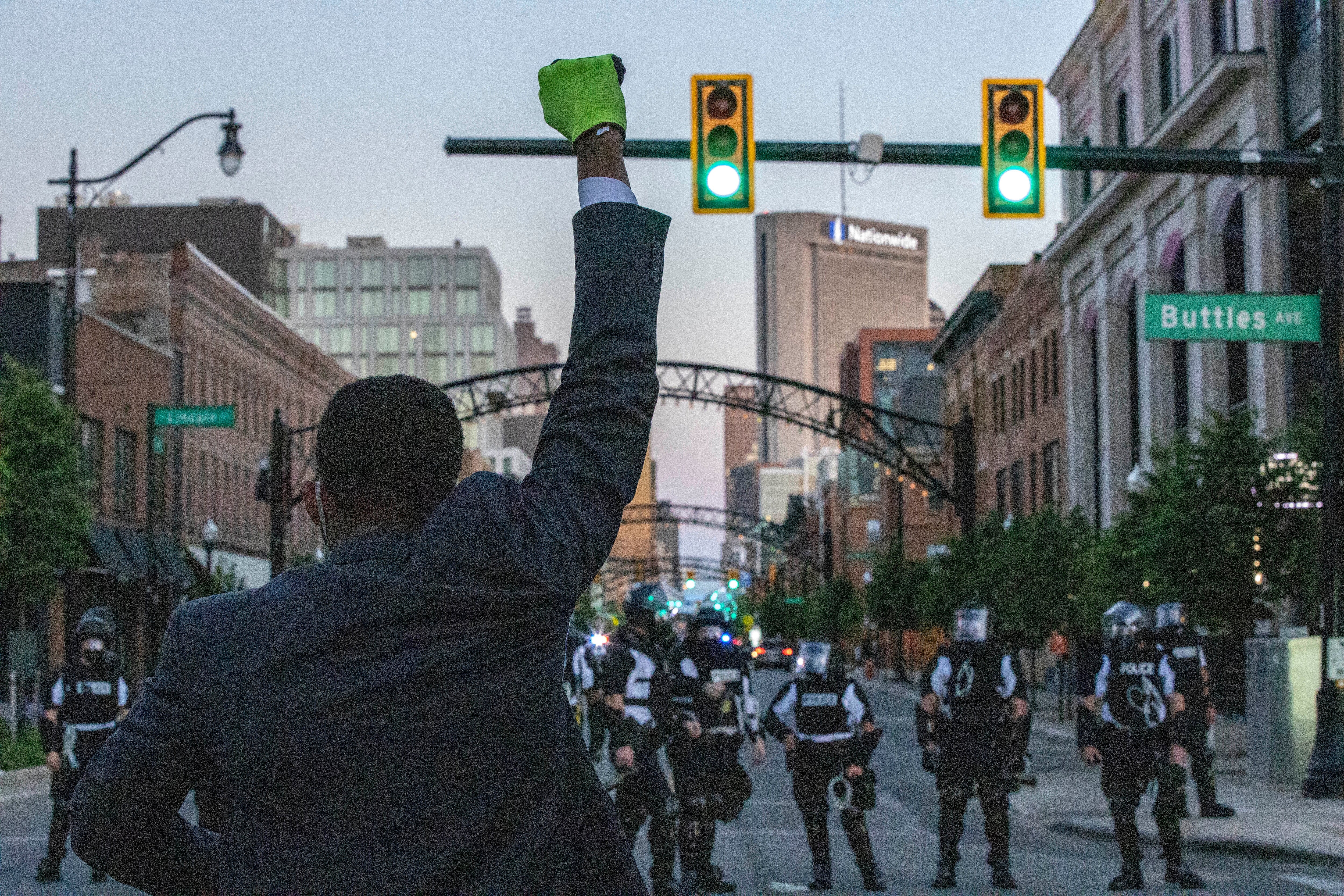 En person i dress hever en knyttneve mot en rekke politifolk i opprørsutstyr i en bygate