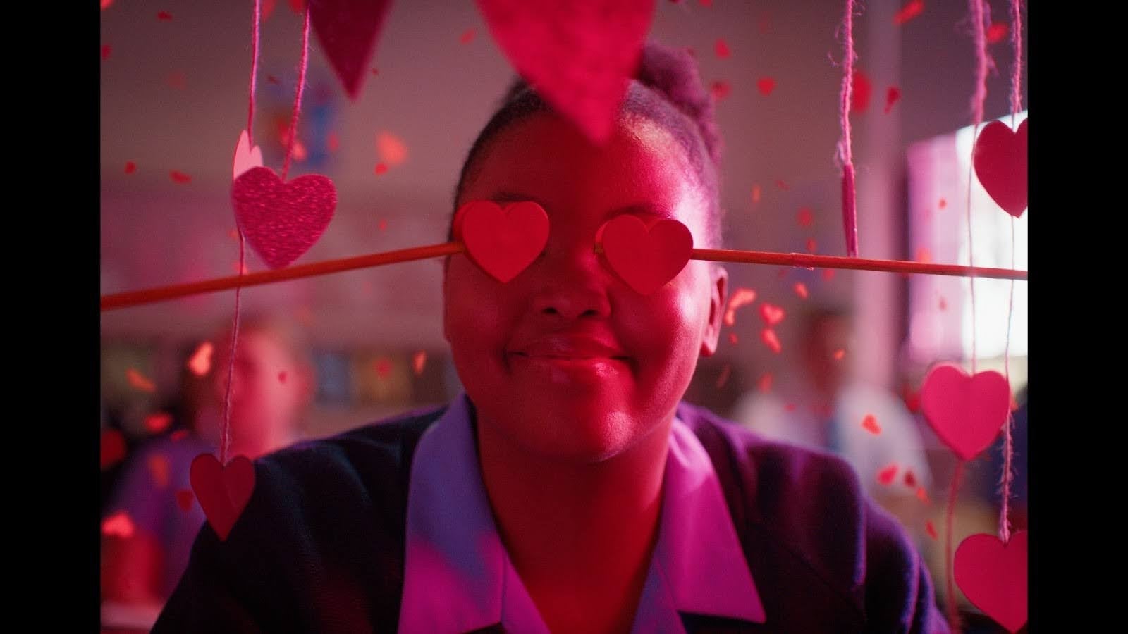 Person smiling behind heart decorations on strings, creating a playful and romantic atmosphere