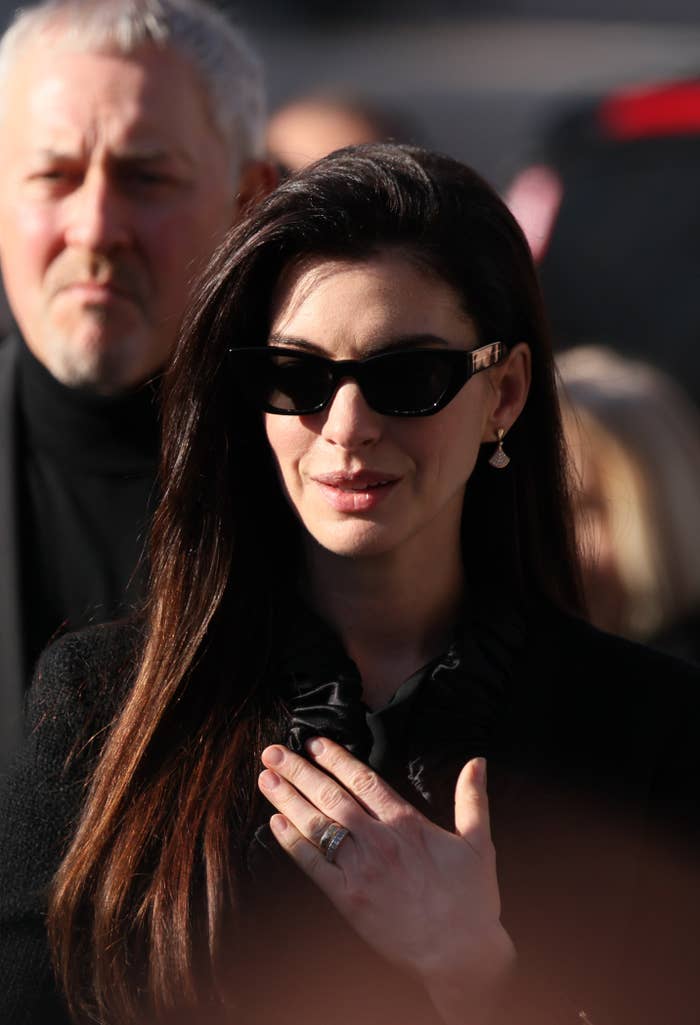 Anne Hathaway successful  sunglasses and chic attire with subtle jewelry attends an lawsuit   outdoors, holding her manus  implicit    her chest