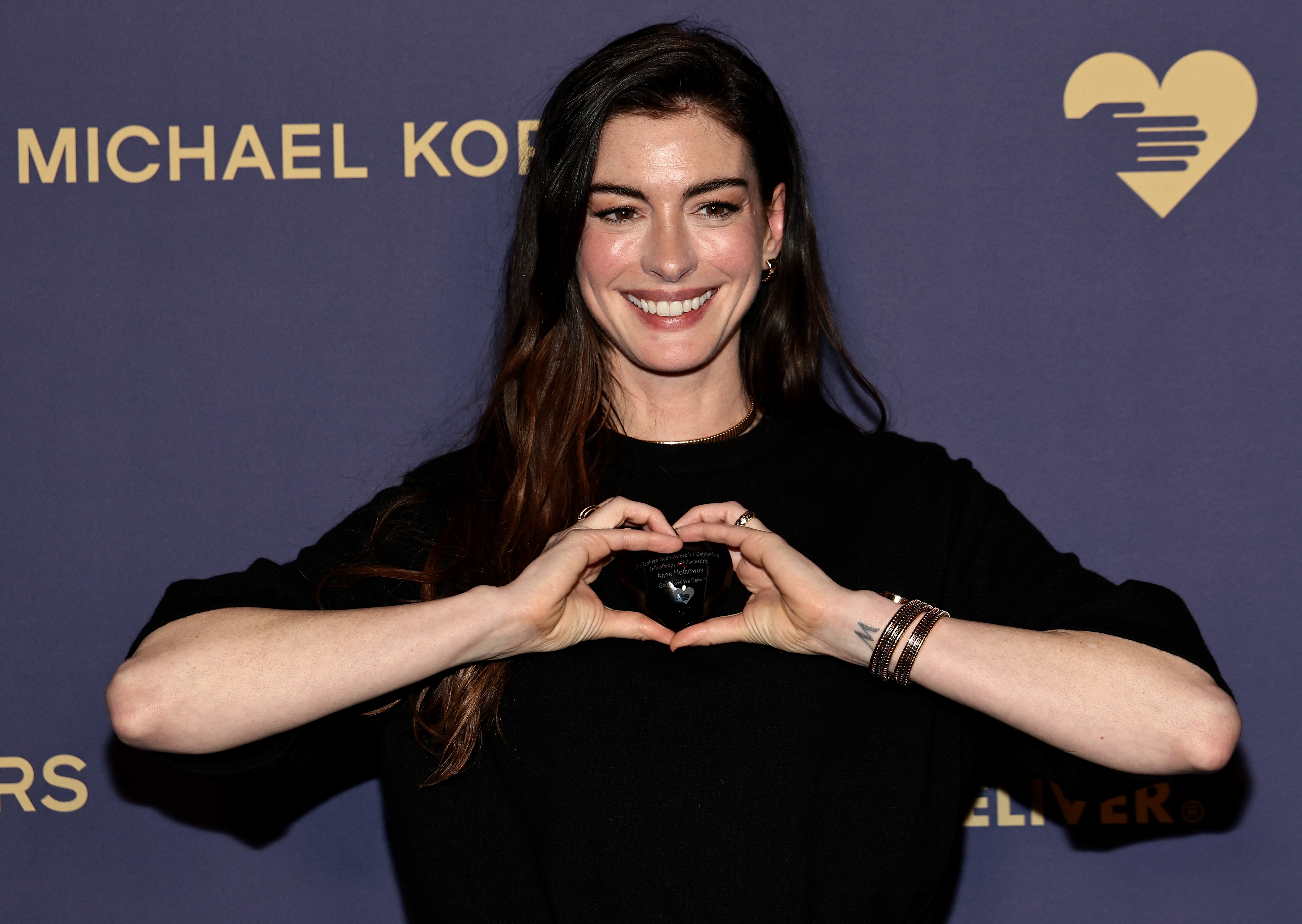 Anne Hathaway smiling, forming a bosom  signifier   with hands, against a backdrop with text