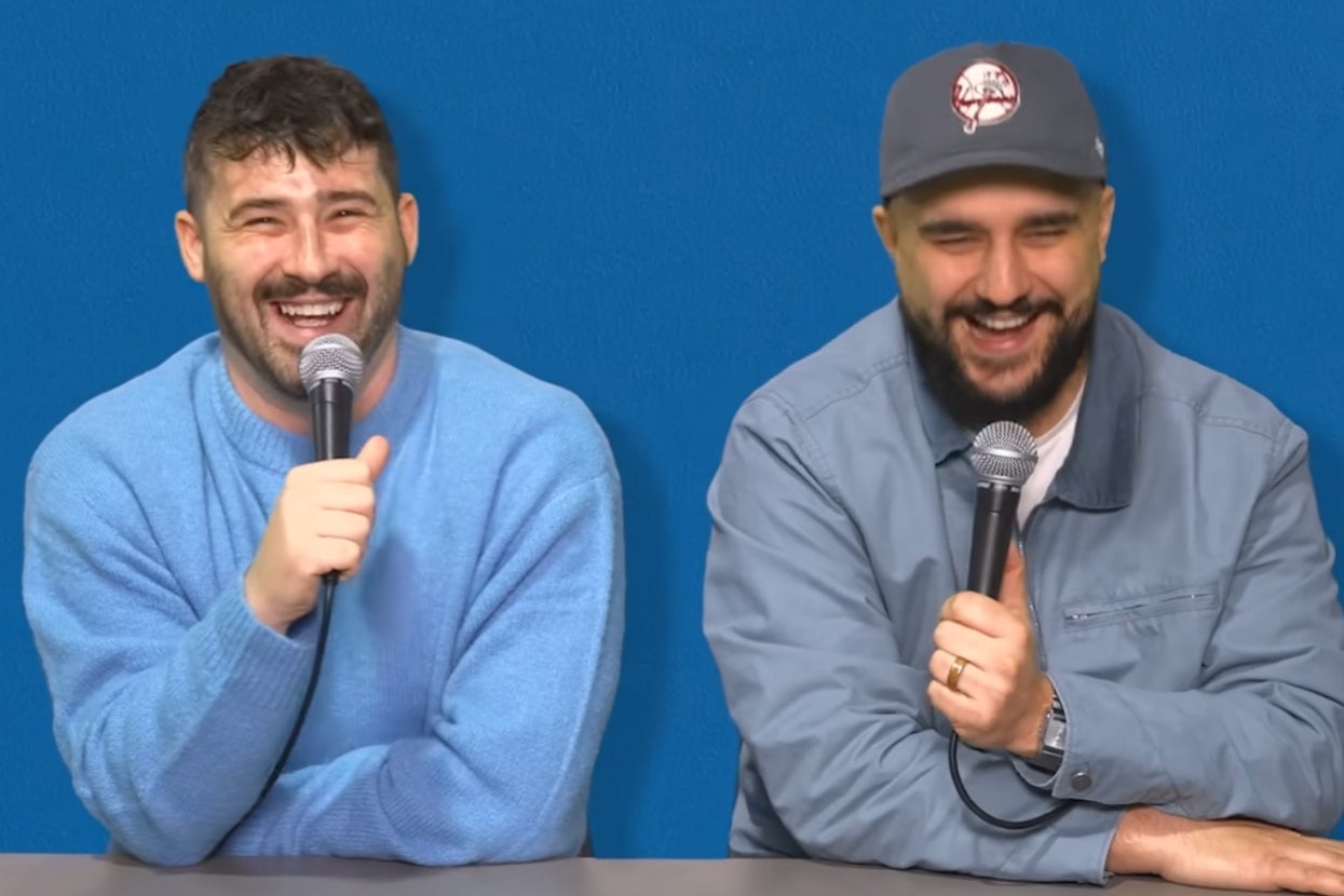 Two people sitting side by side, holding microphones, smiling and laughing during a casual interview or podcast setting