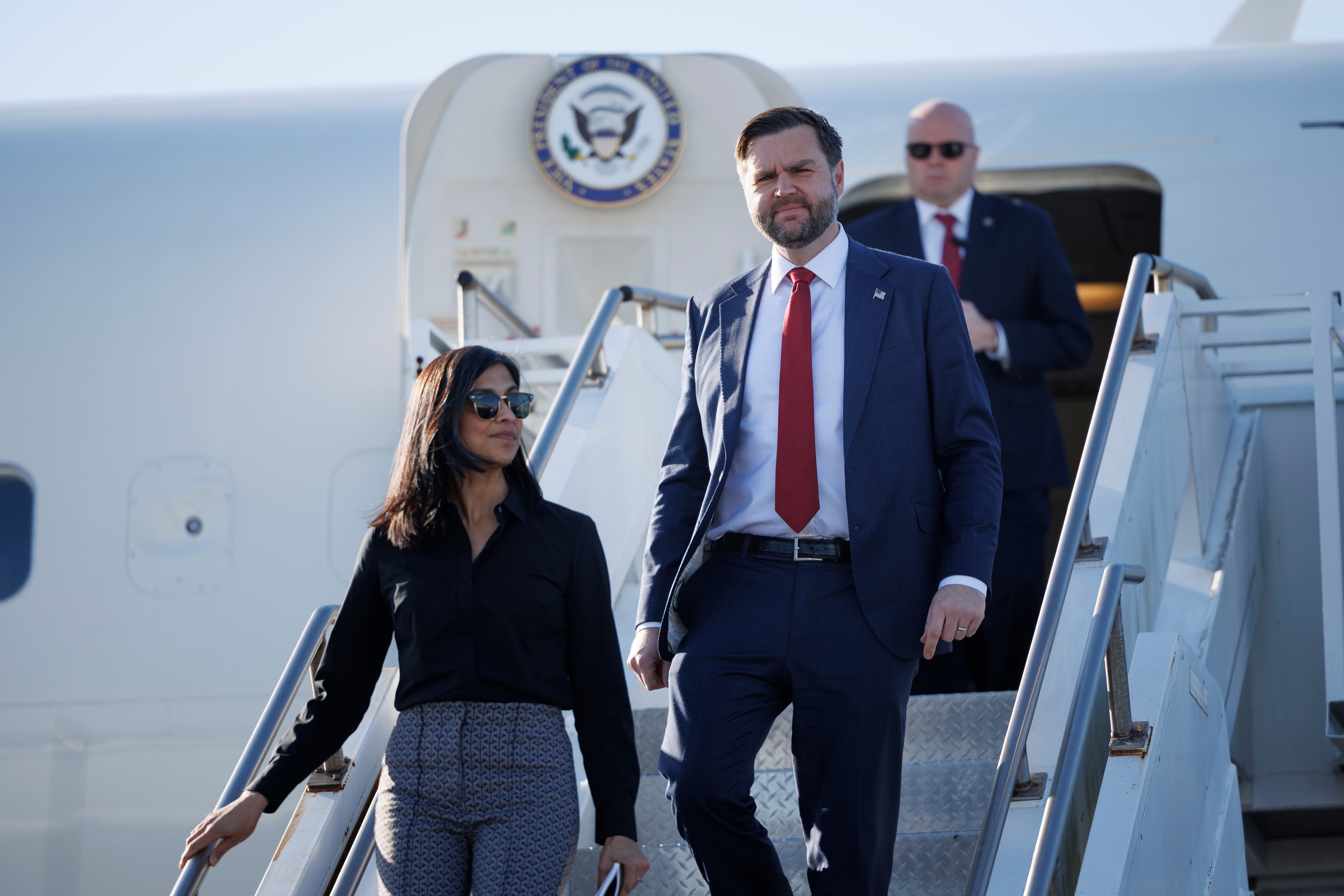 A antheral and pistillate successful concern attire exit a plane. The antheral wears a suit and tie, the pistillate wears a blouse and pants. A 3rd idiosyncratic follows behind