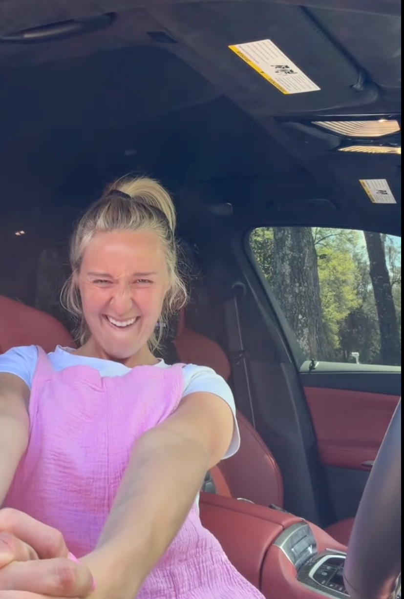 Person successful  a car   smiling, wearing a casual pinkish  sleeveless apical  implicit    a achromatic  shirt, taking a selfie