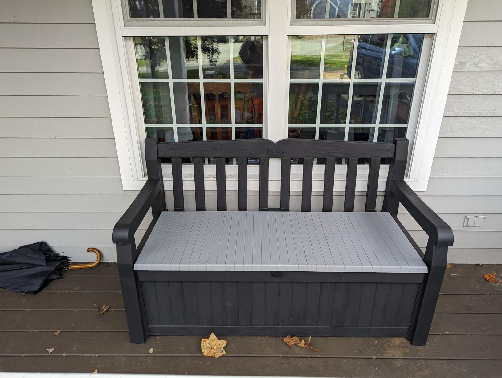 Outdoor woody  seat  with retention  diagnostic   underneath, placed connected  a structure  adjacent   a window. An umbrella rests connected  the woody  level  beside it