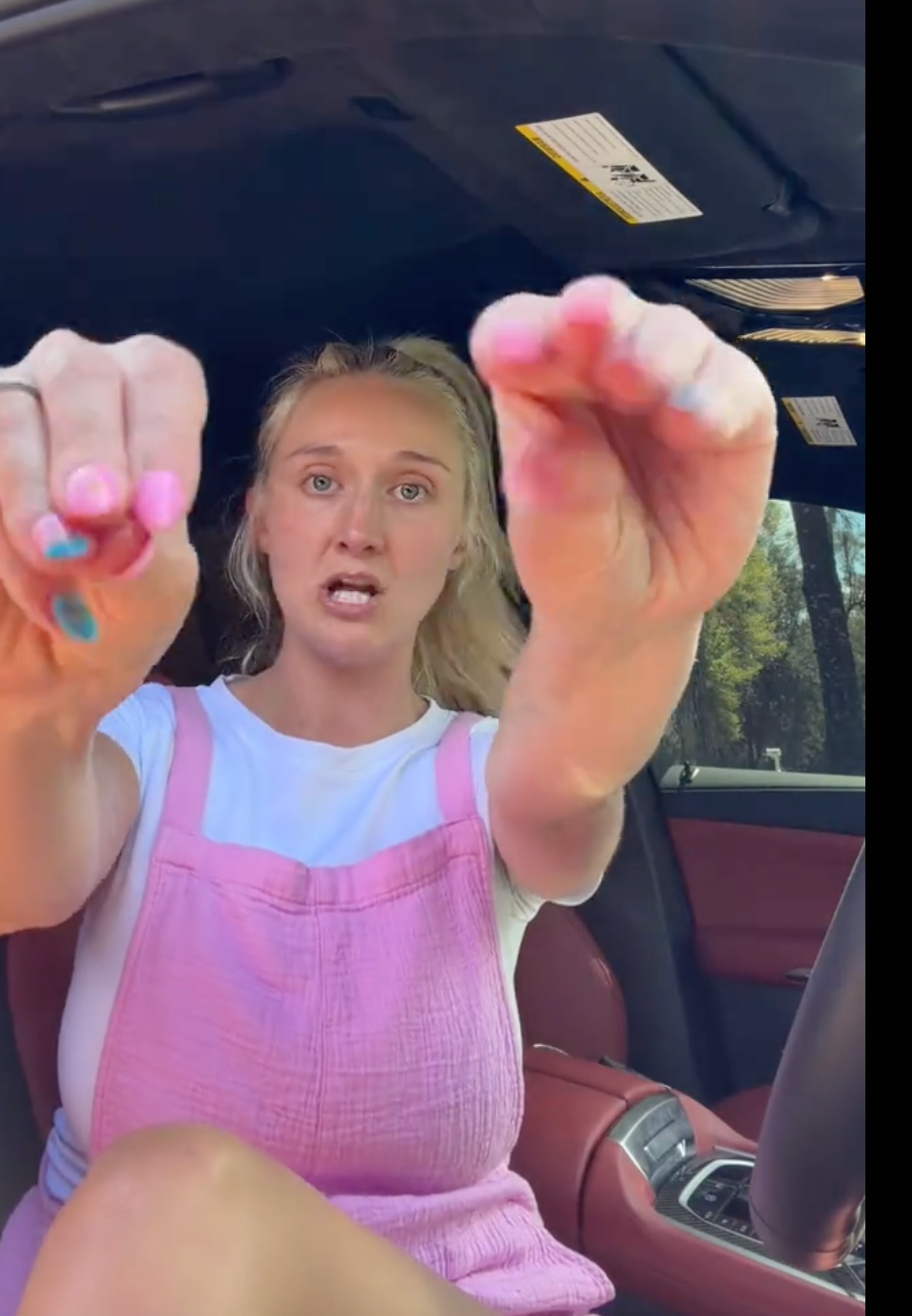 Person sitting successful  a car, wearing a achromatic  garment  and pinkish  overalls, gesturing with hands outward